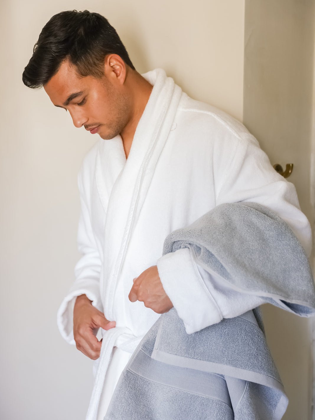 Man in white robe holding harbor mist luxe bath towel 