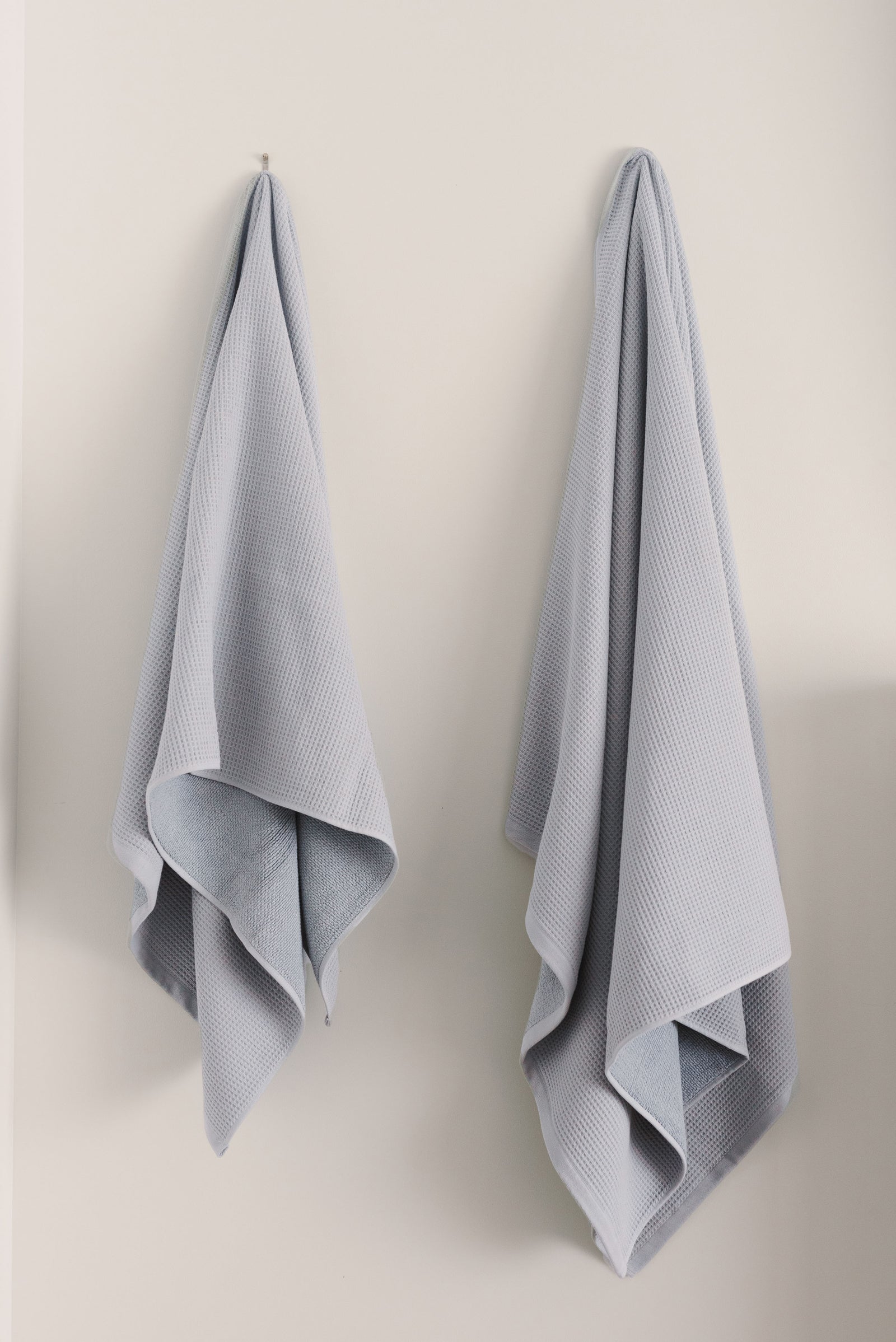 Waffle Bath Towel in the color Harbor Mist. Photo of Harbor Mist Waffle Bath Towel taken hanging from a towel hook in a white bathroom.