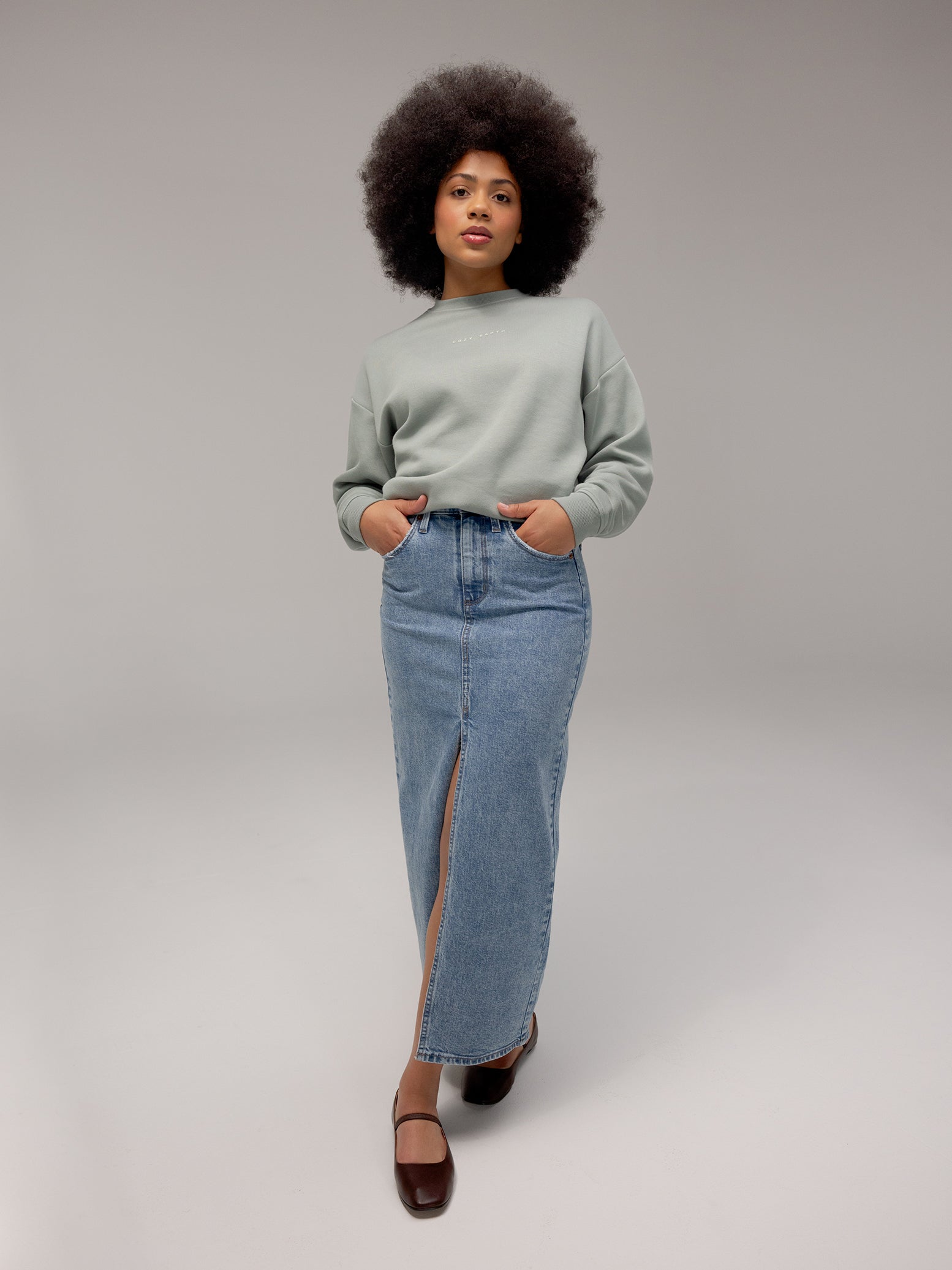 Haze CityScape Pullover Crew. The Pullover is being worn by a female model. An accompanying jean skirt is being worn to complete the look of the outfit. The photo was taken with a white background.