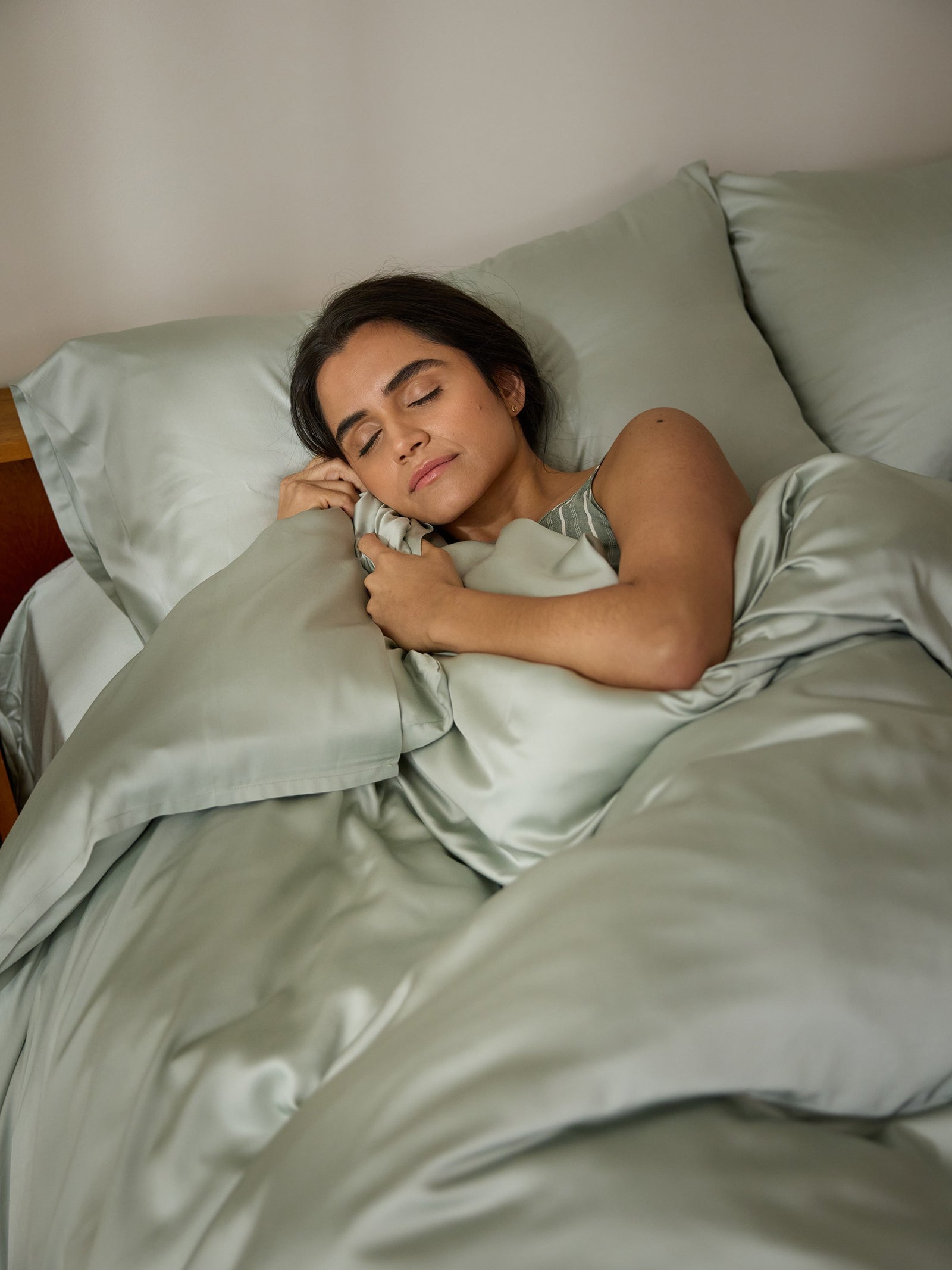 A woman peacefully sleeps in a bed with a Cozy Earth Bamboo Duvet Cover and matching pillowcases, clutching one pillow close. The setting conveys comfort and tranquility.