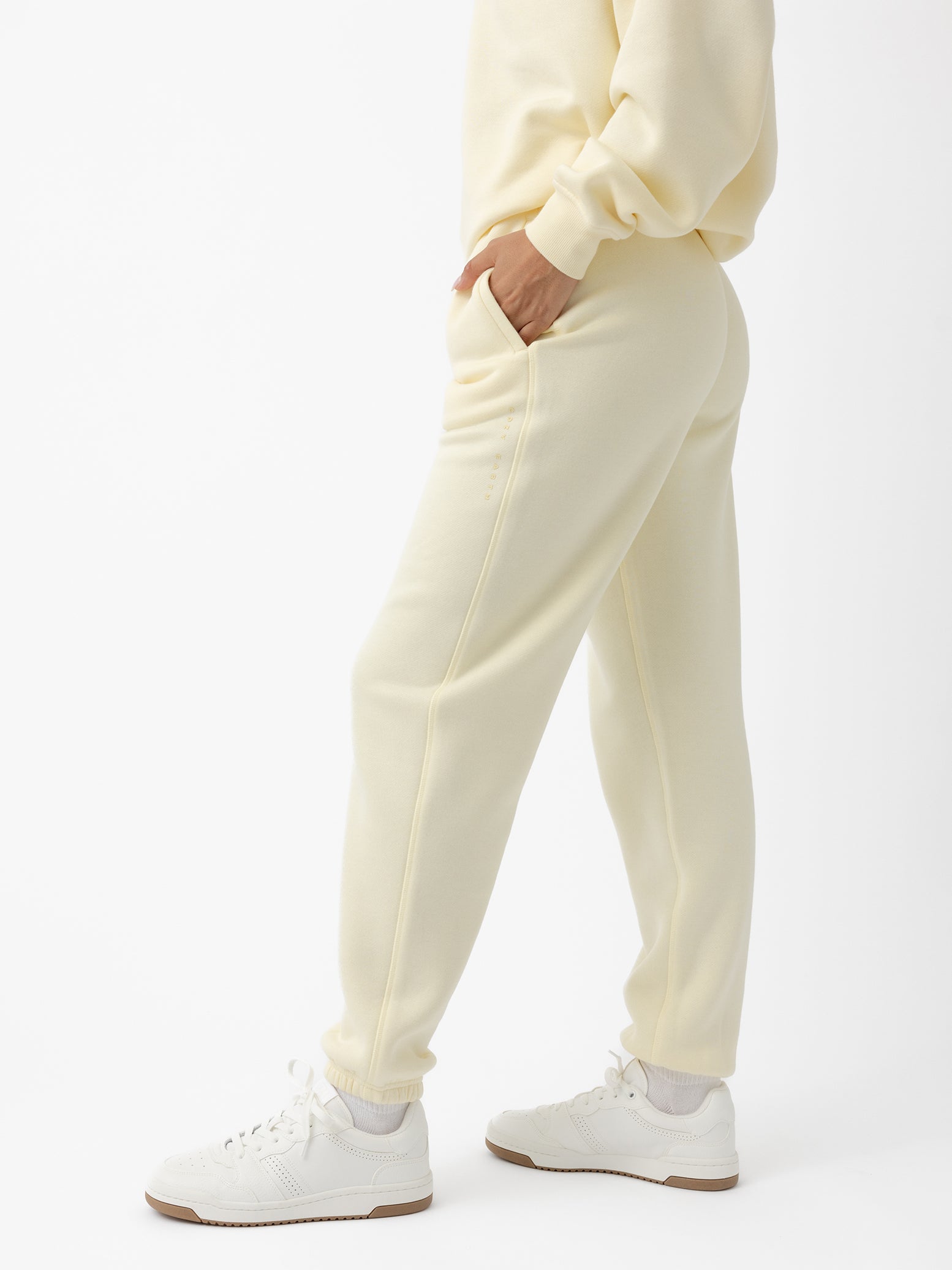 A person wearing Cozy Earth's Women's CityScape Sweatpant in lemonade stands sideways with hands in pockets and pairs the look with white sneakers against a white background, offering a comfortable and casual vibe.