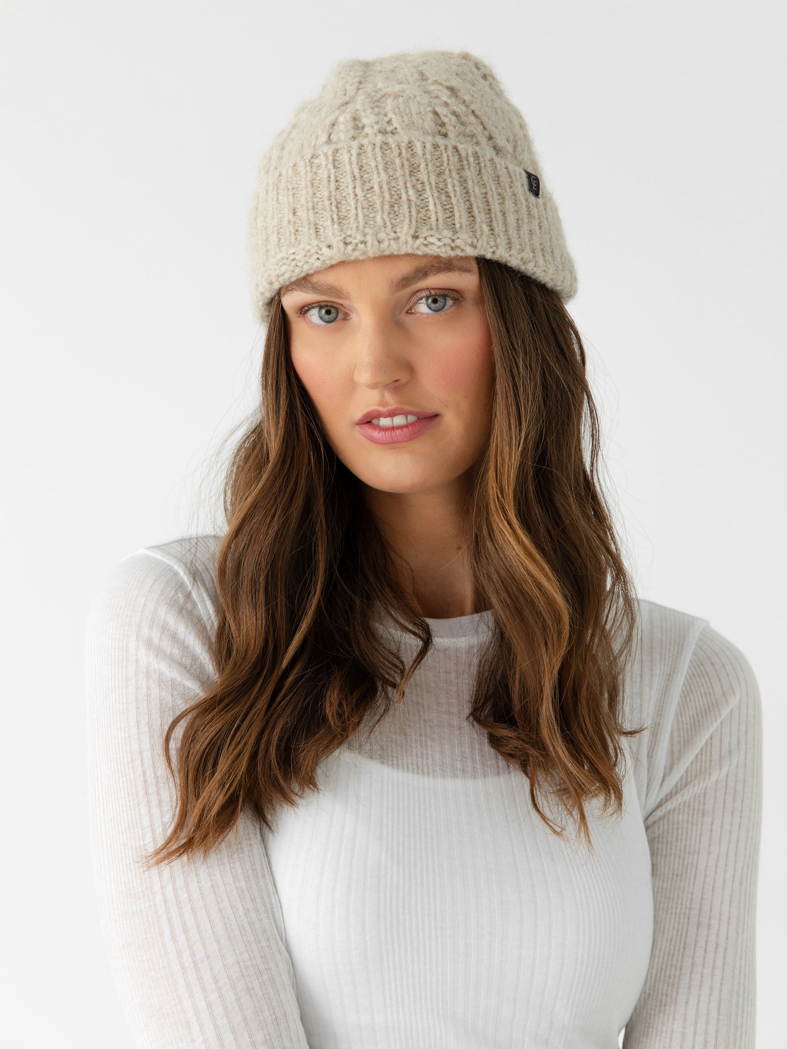 Woman wearing a tan Cozy Earth Cable Knit Beanie and scarf in front of a white background.