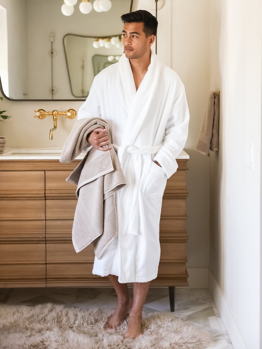 Man in white robe holding sand luxe bath sheet 