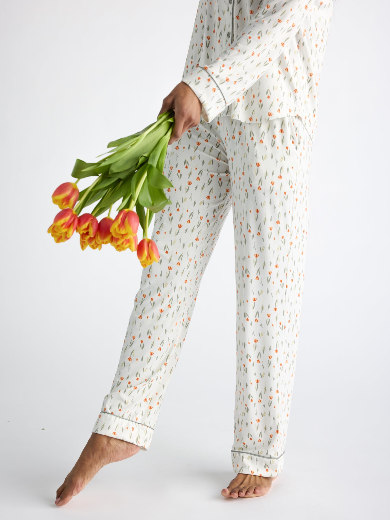 A person wearing Cozy Earth Women's Bamboo Stretch-Knit Pajama Pant holds orange and yellow tulips, standing barefoot against a white background.