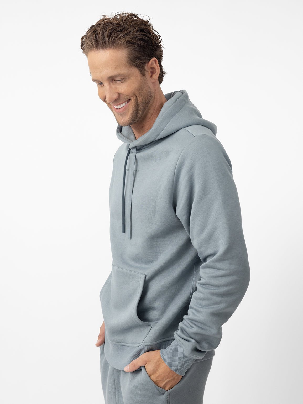 Man smiling wearing smokey blue cityscape hoodie with white background