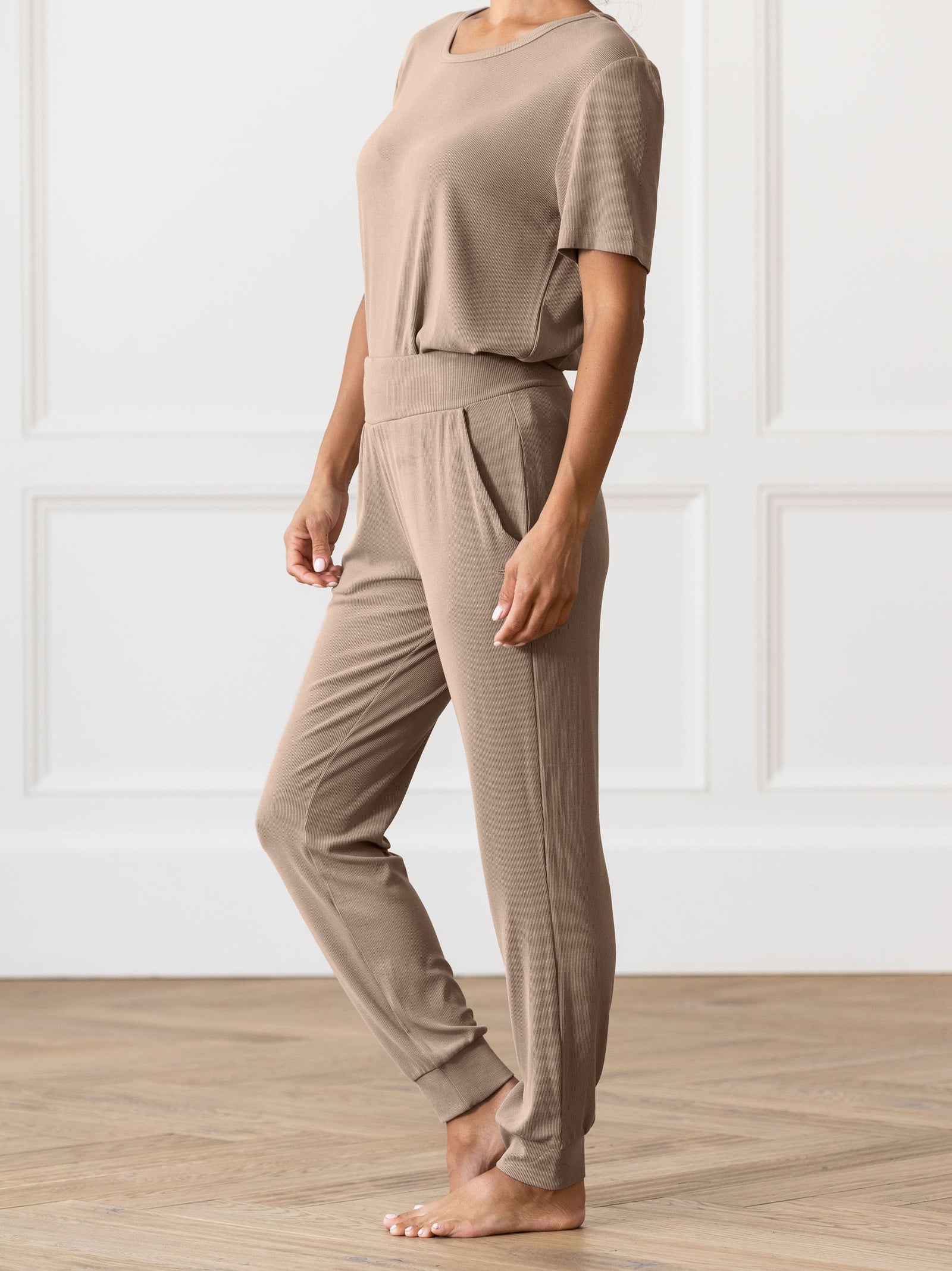 Person wearing beige Cozy Earth Rib Knit Joggers on a wooden floor with a white paneled wall background