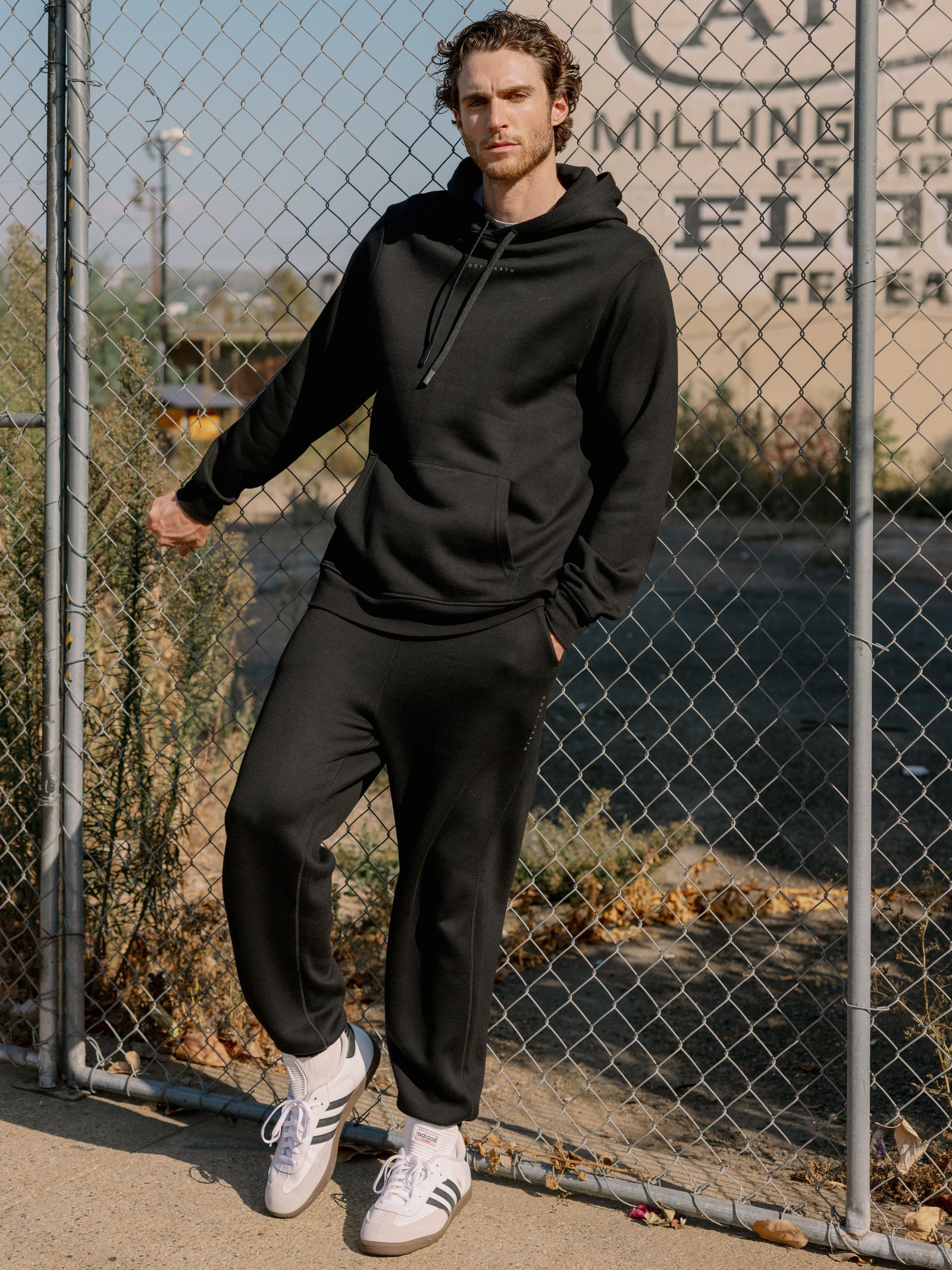 Man next to fence wearing black cityscape sweats and hoodie