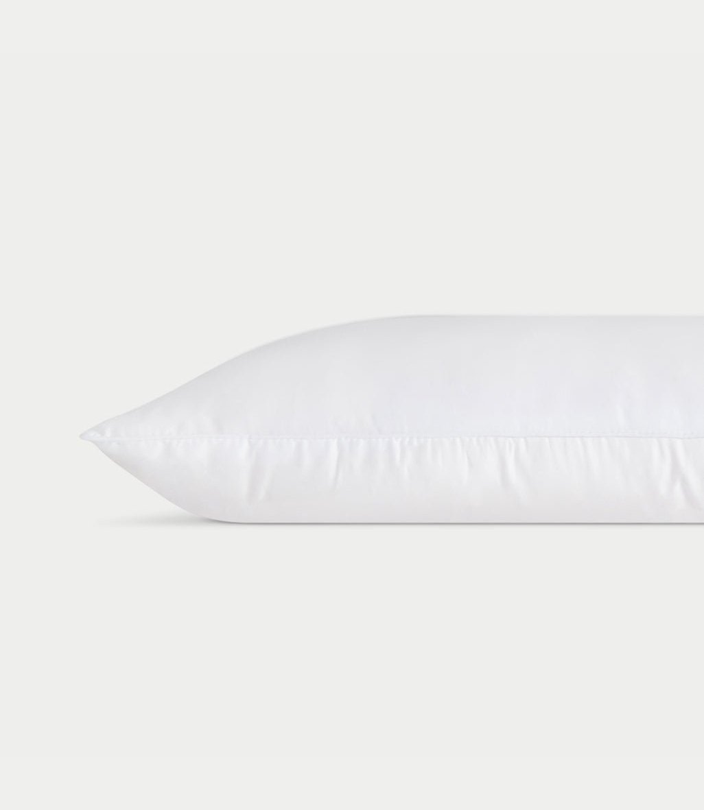 A white **Silk Pillow** from **Cozy Earth** lies horizontally against a plain white background, showcasing a clean and smooth surface with faint stitching along the edge, giving it a fresh and fluffy appearance.
