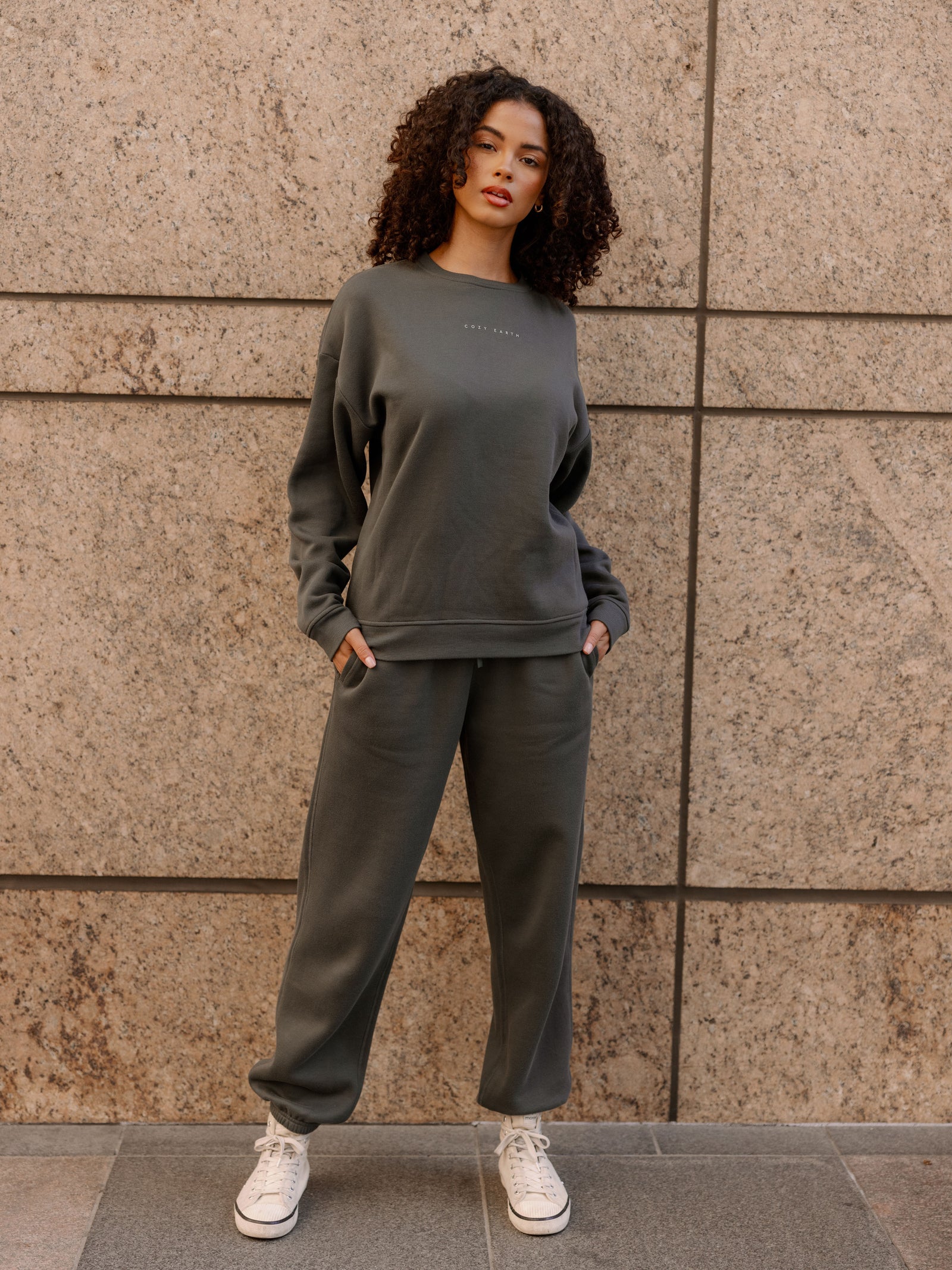 Storm CityScape Pullover Crew. The Pullover is being worn by a female model. Accompanying city scape clothing is being worn to complete the look of the outfit. The photo was taken with a city building background.