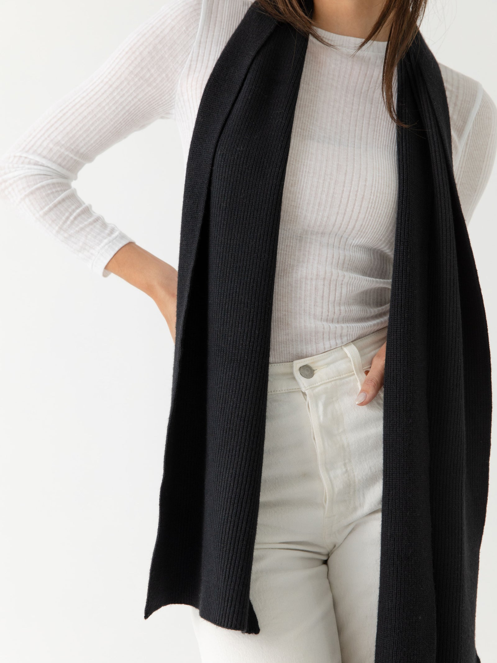 Person wearing a black scarf, white sweater, and light-colored pants on a white background