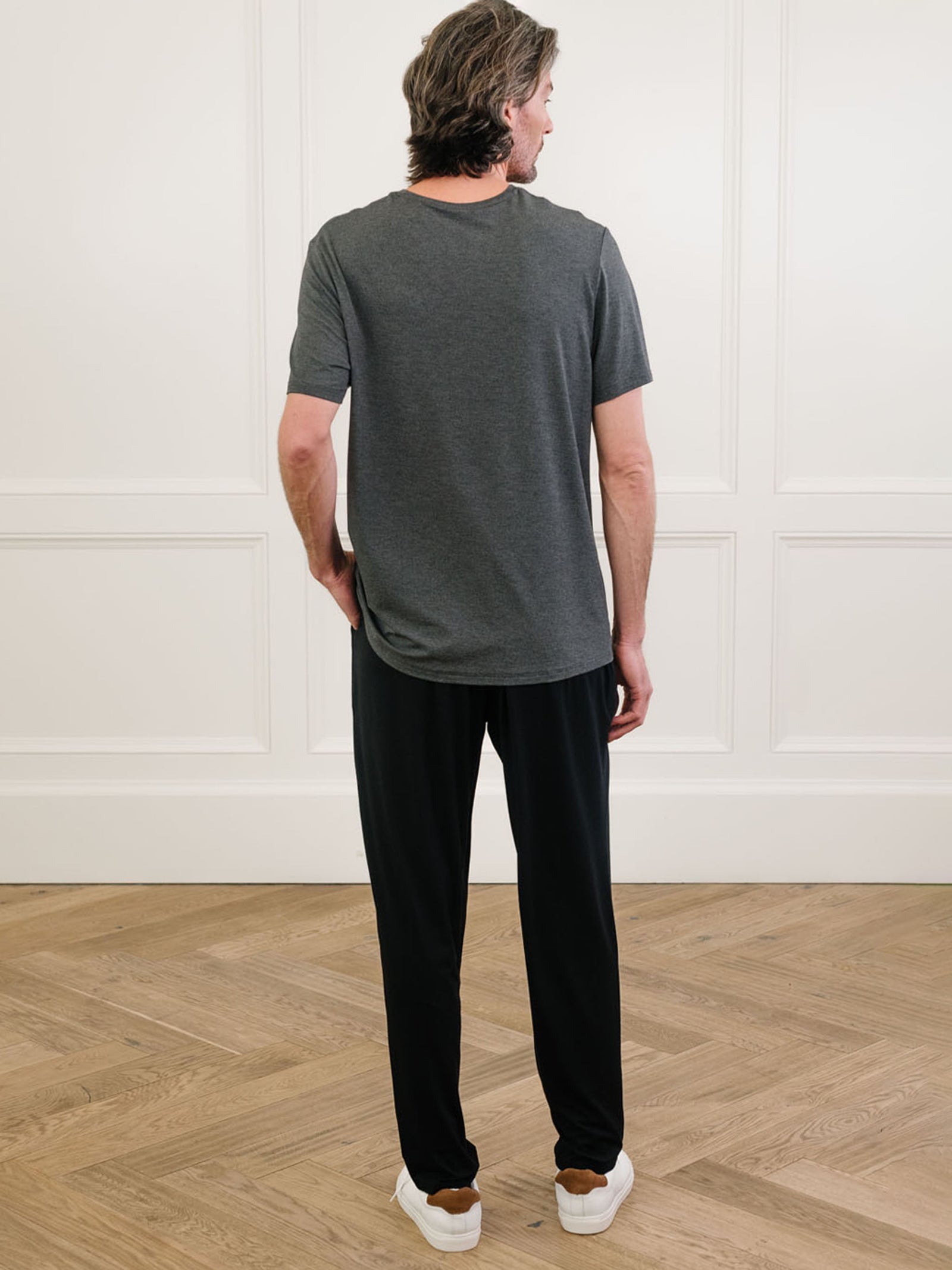 Charcoal Men's Stretch-Knit Bamboo Lounge Tee. A man is wearing the lounge tee in a well lit home with his back facing the camera.