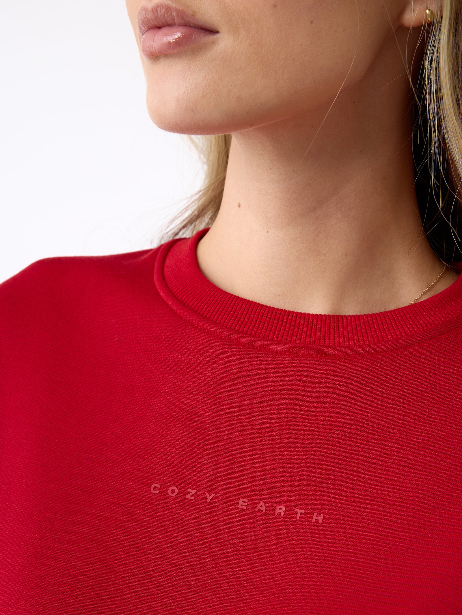Close-up of a person wearing a red Women's CityScape Crewneck by Cozy Earth. The focus is on the neck and shoulders, showing minimal facial features against a plain white background.