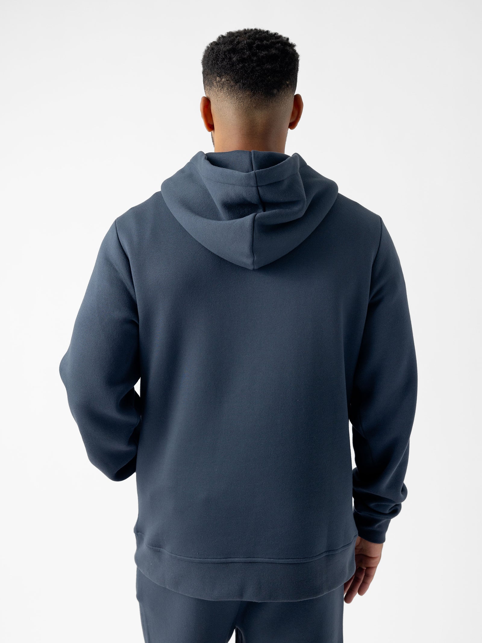 A person with short hair is seen from behind wearing a dark, long-sleeved Men's CityScape Hoodie by Cozy Earth. The background is plain and white.
