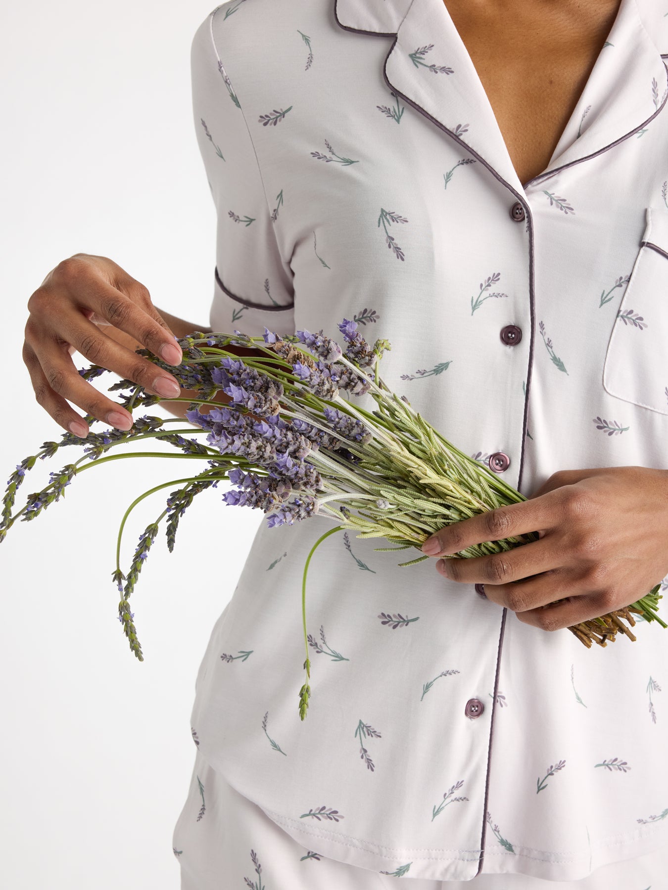A woman in HIDE's Women's Bamboo Stretch-Knit Short Sleeve Pajama Top, inspired by lavender, holds a bunch of fresh lavender flowers.