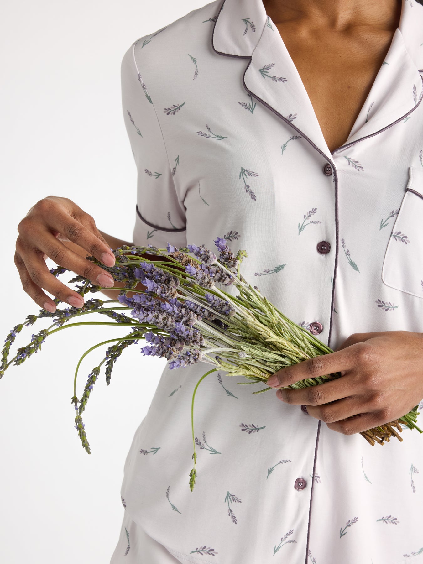 A person in Cozy Earth's Women's Bamboo Stretch-Knit Short Sleeve Pajama Set with a lavender pattern holds fresh lavender sprigs against a plain background.