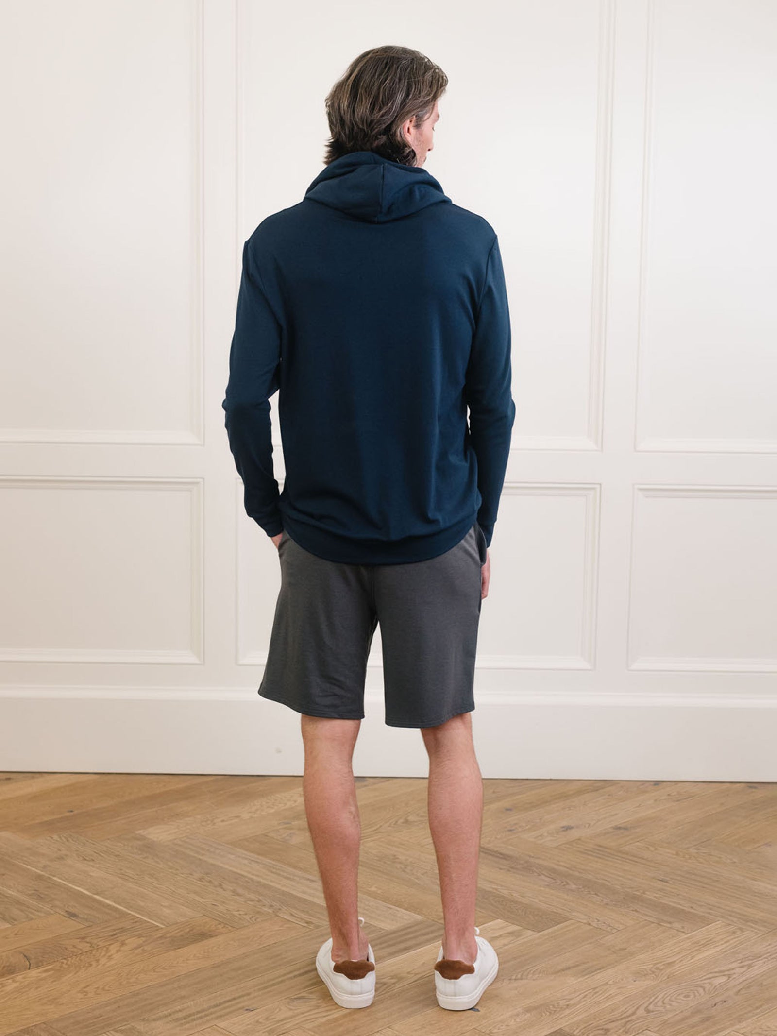 Navy Bamboo Hoodie worn by man standing in front of white background with his back facing the camera.