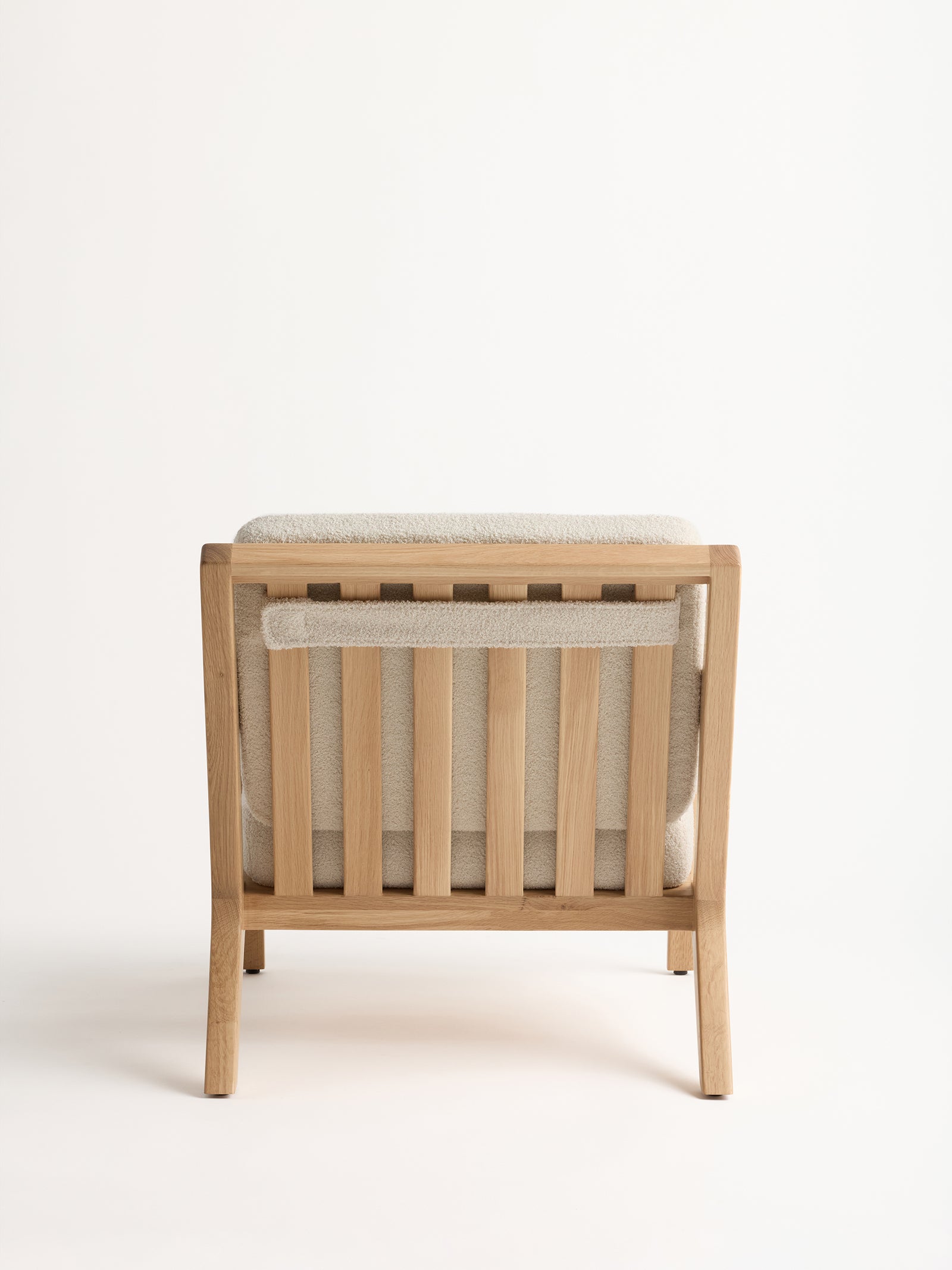 The Coronado Lounge Chair by Cozy Earth is displayed from the back, showcasing its simple, modern wooden design with vertical slats and a light beige cushion on the seat and backrest, all set against a neutral background.