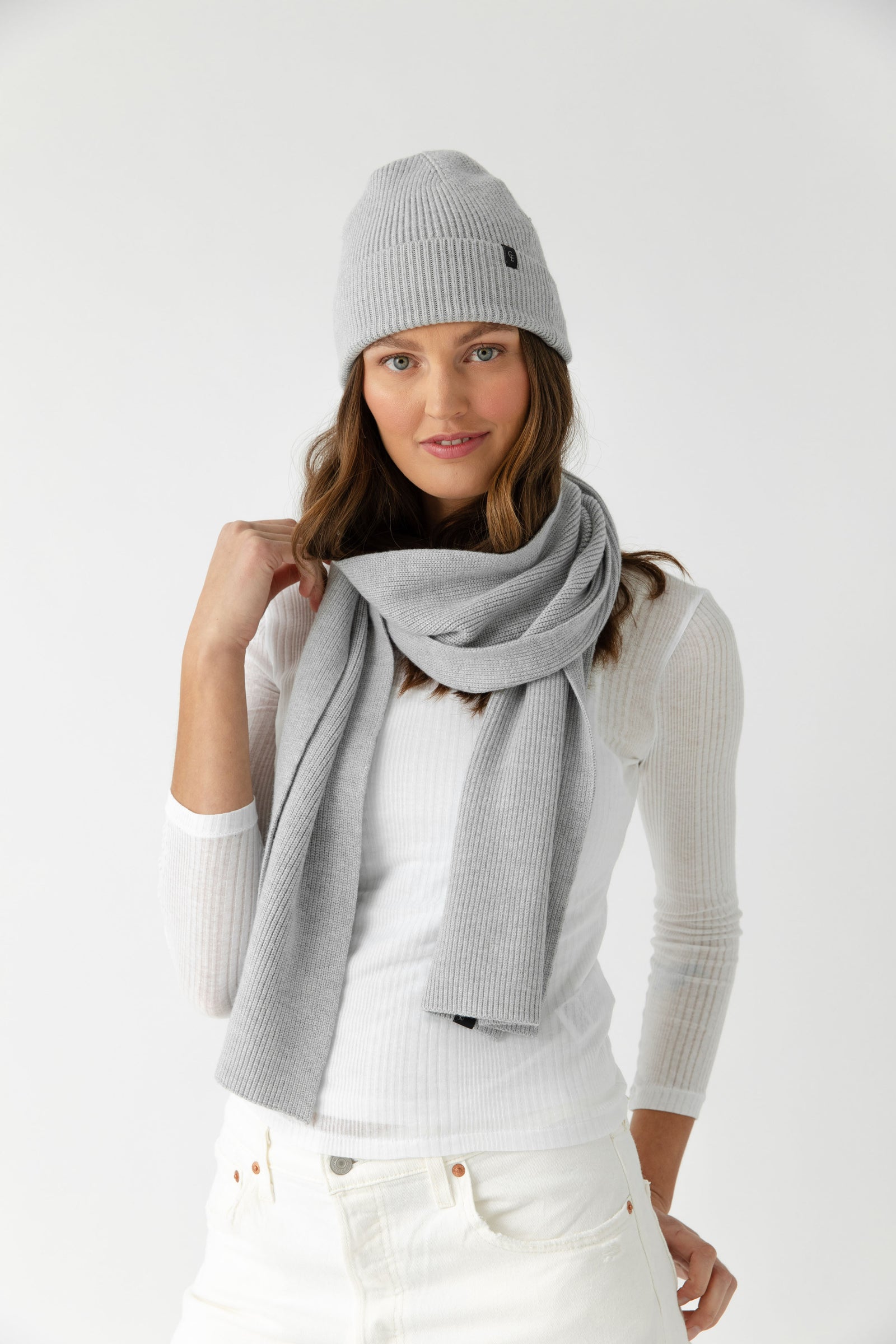 Person wearing a light grey scarf, white sweater, and light-colored pants on a white background