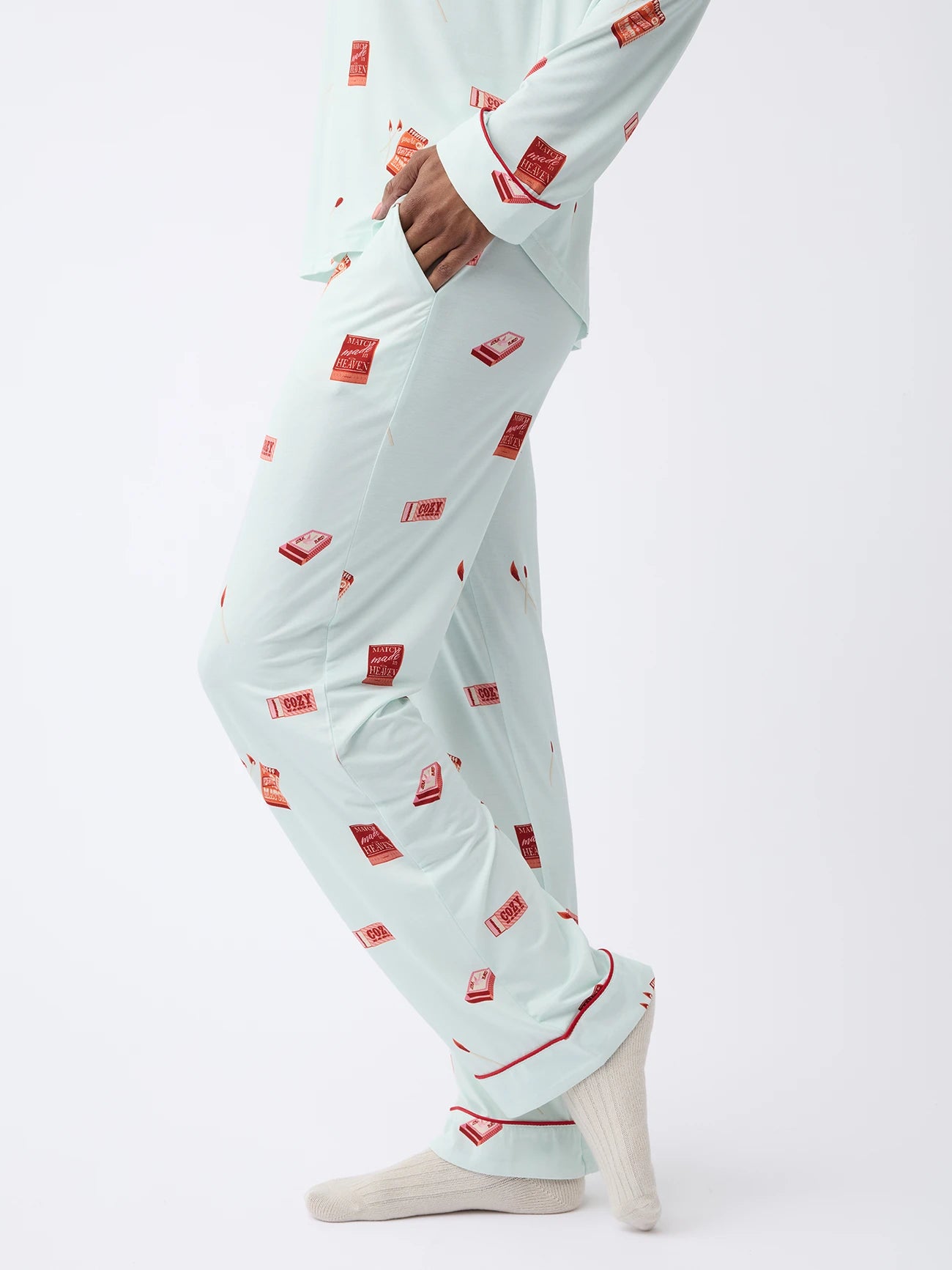 A person in Cozy Earth Women's Stretch-Knit Bamboo Pajama Pant, light blue with red and white match books, stands on a white backdrop.