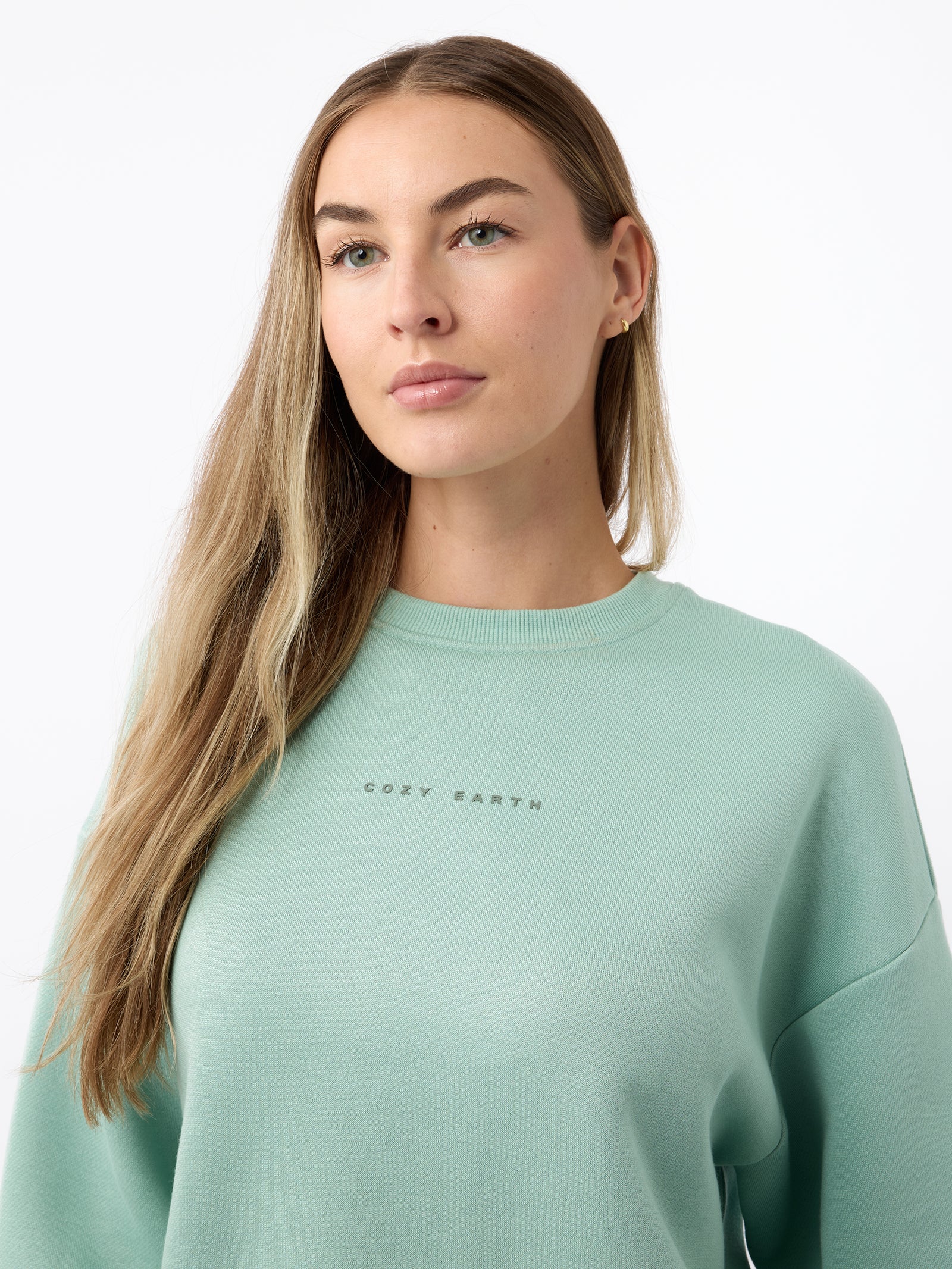A person with long hair wearing a light green Women's CityScape Crewneck from Cozy Earth stands against a plain white background.