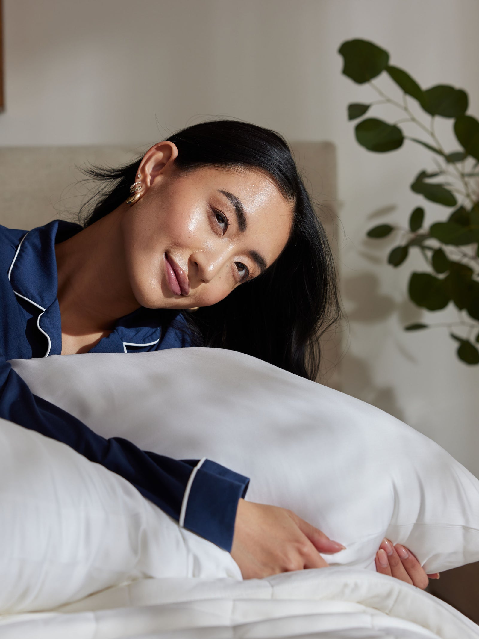 Woman sitting on bed holding down pillow sizes standard and king