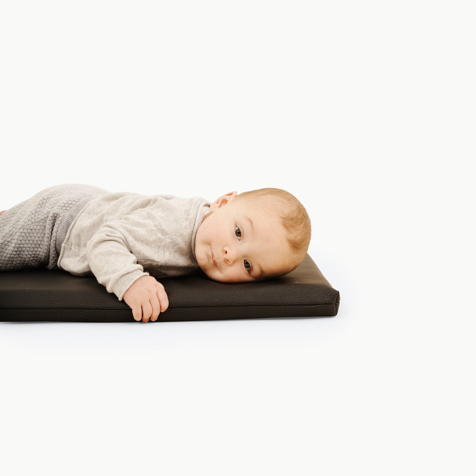 A baby in light clothes rests calmly on a black Gathre Wholesale Padded Changing Mat against a plain white background.