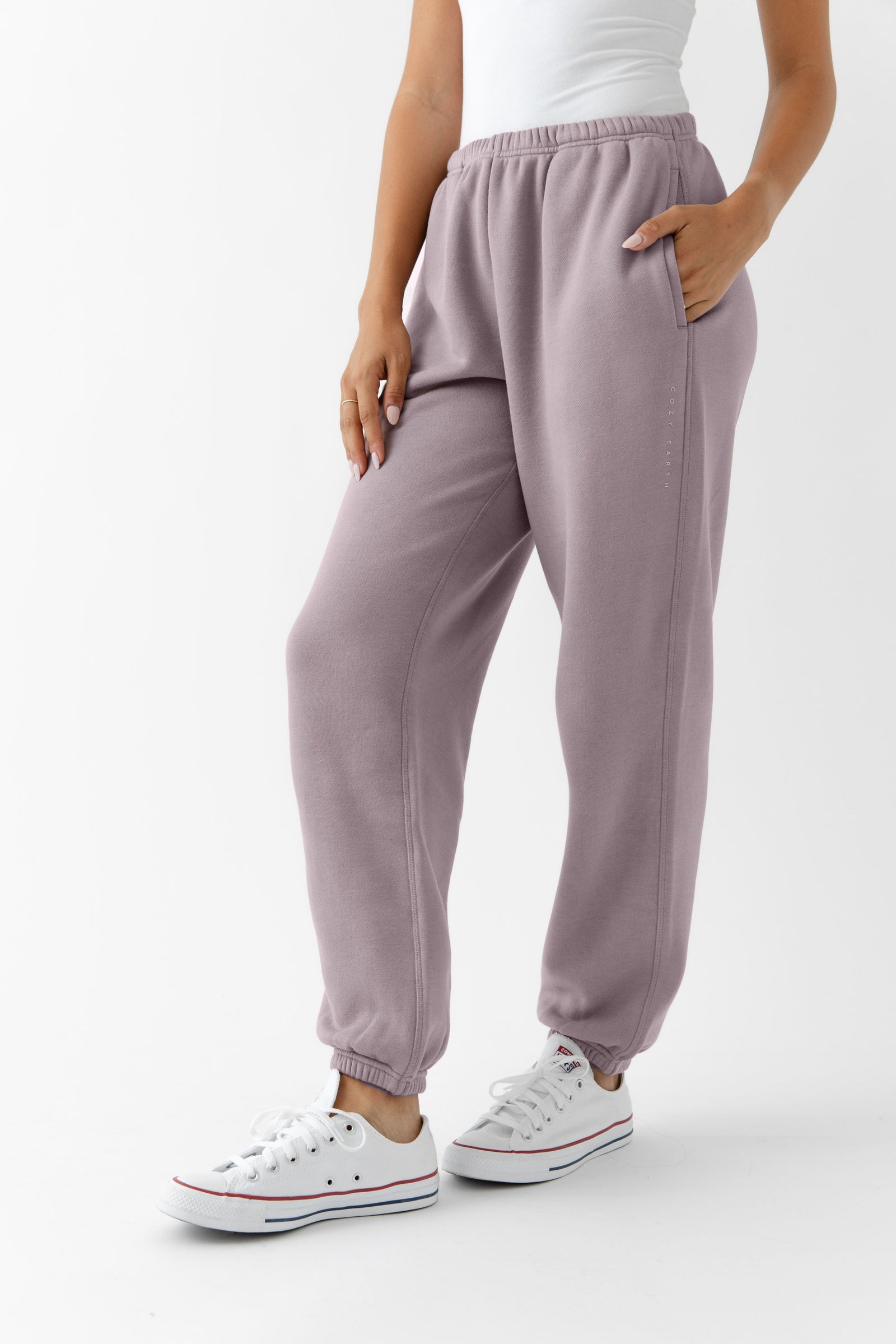 Dusty Orchid CityScape Joggers. The Joggers are being worn by a female model. The photo is taken from the waist down with the models hand in the pocket of the joggers. The back ground is white.