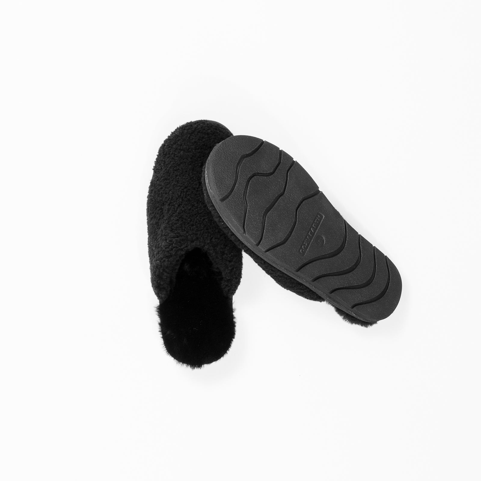 A pair of Puffy Sheep Slippers by Cozy Earth arranged on a white background. One slipper is placed with the sole facing up, showing its textured, wavy pattern, while the other is positioned to display the plush, furry interior.