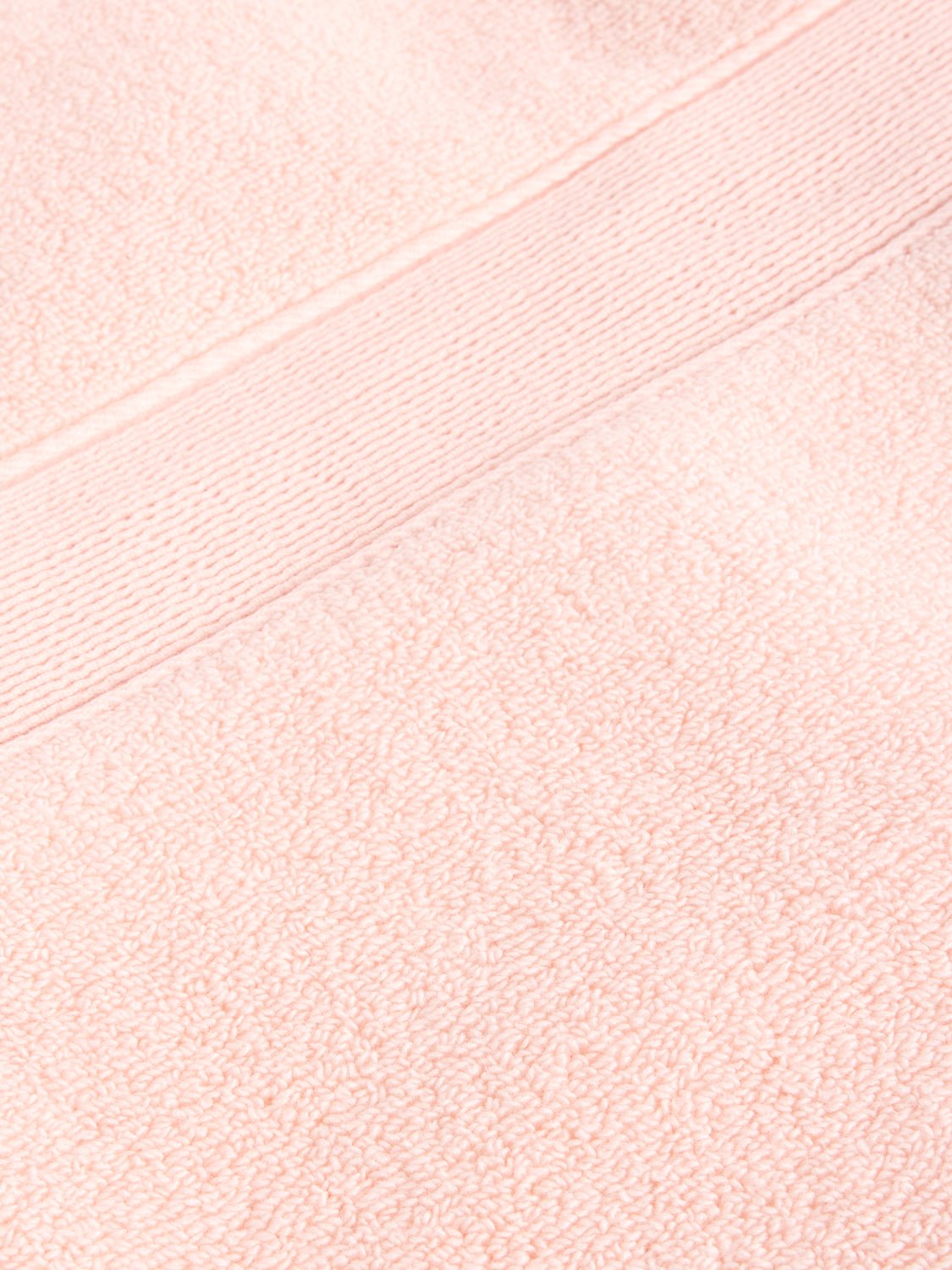 Close-up of a Luxe Bath Towel by Cozy Earth in light pink, featuring a fluffy texture with a horizontal band design near the top edge.