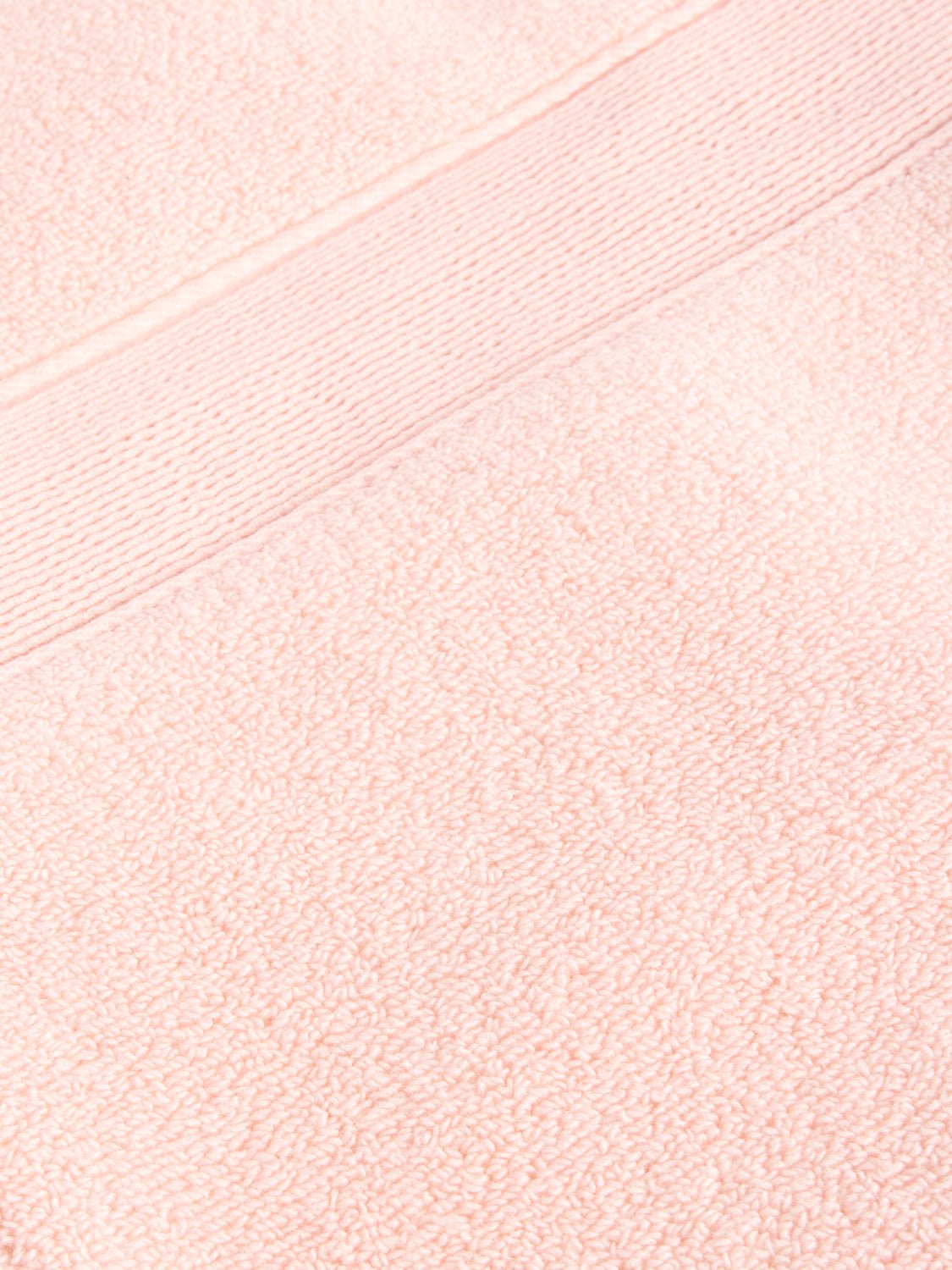 A close-up of a Luxe Washcloth by Cozy Earth reveals the textured fabric in soft, pastel pink, featuring a smooth horizontal band with a fine line pattern running across it.