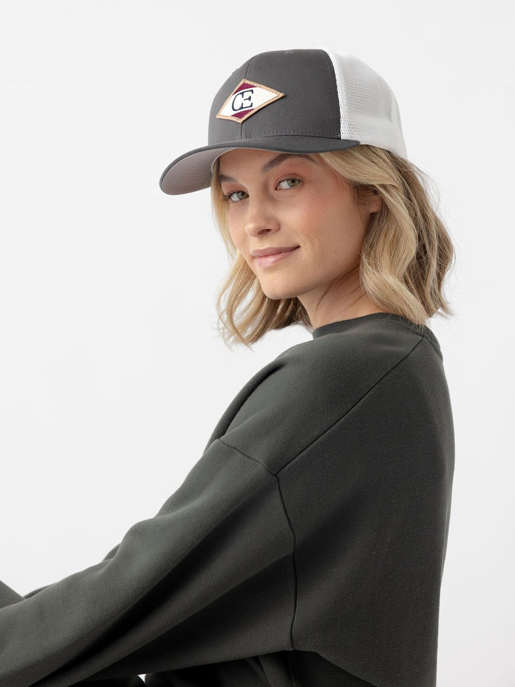 Woman looking at camera wearing charcoal/white diamond mesh trucker hat