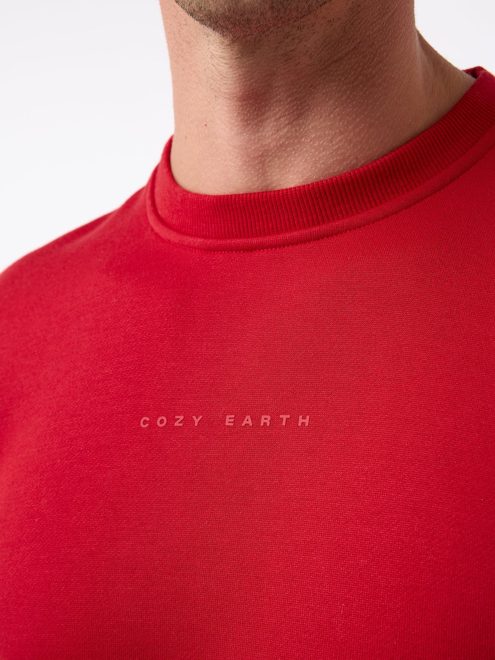 Close-up of a person wearing the Men's CityScape Crewneck in red, featuring the brand name "Cozy Earth" printed in small white letters. The focus is on the textured fabric and subtle design.