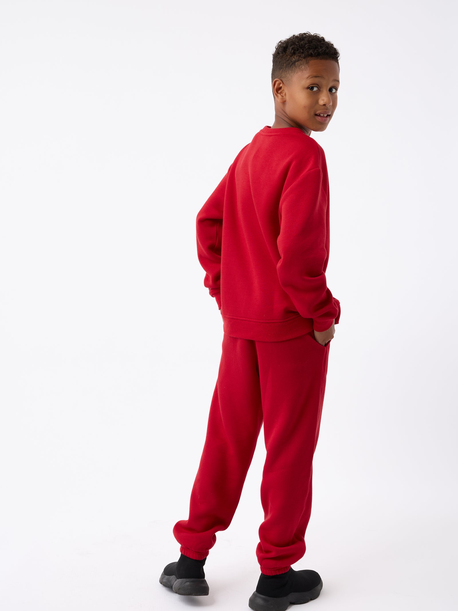 A child dressed in Cozy Earth's Kid's CityScape Sweatpant and black shoes stands against a white background, looking over their shoulder.