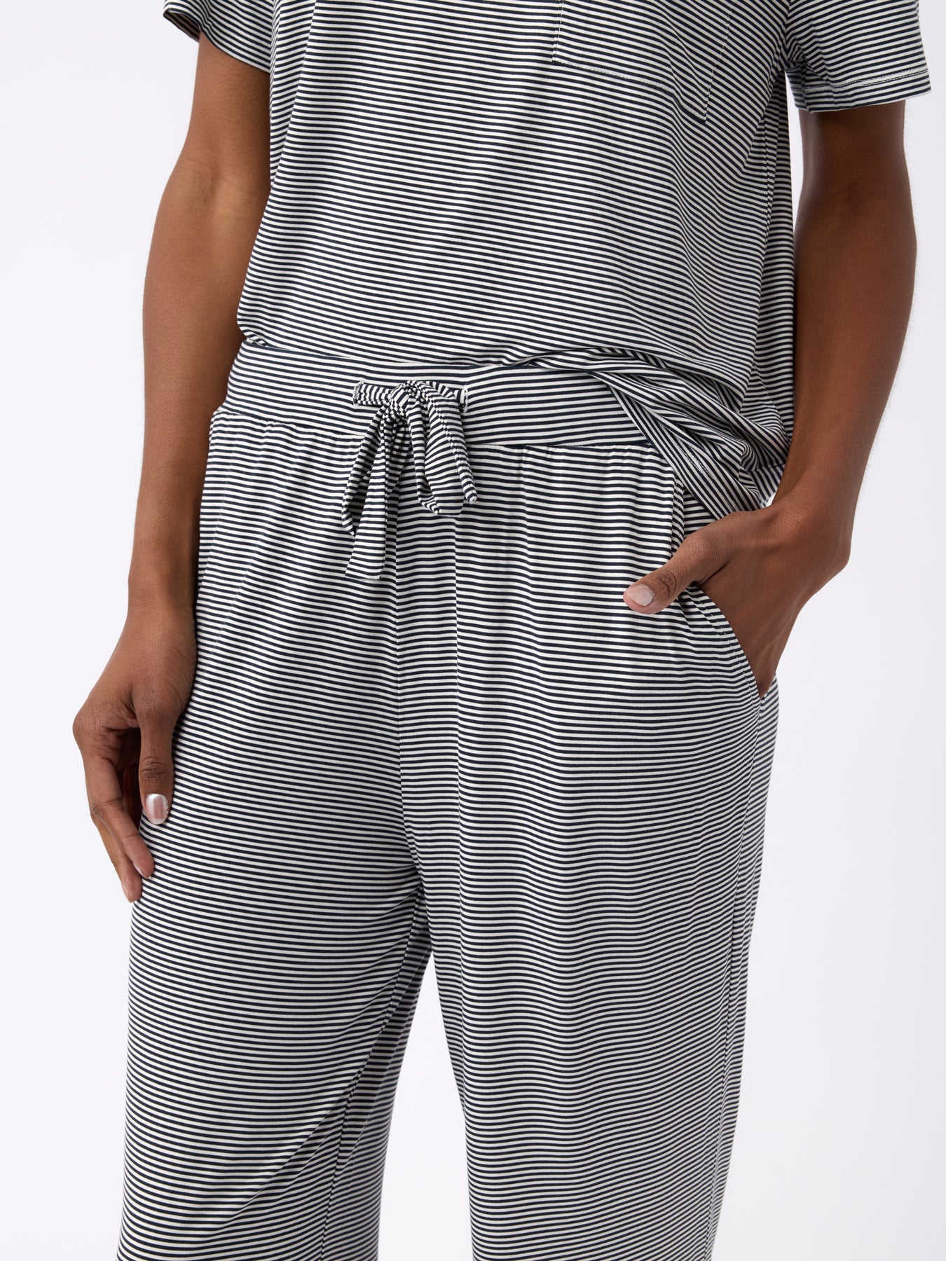 A person is wearing a gray and white striped, short-sleeve shirt with a tied waist, paired with Cozy Earth's Women's Bamboo Stretch-Knit Pant. Their hands are in their pockets against a plain white background.