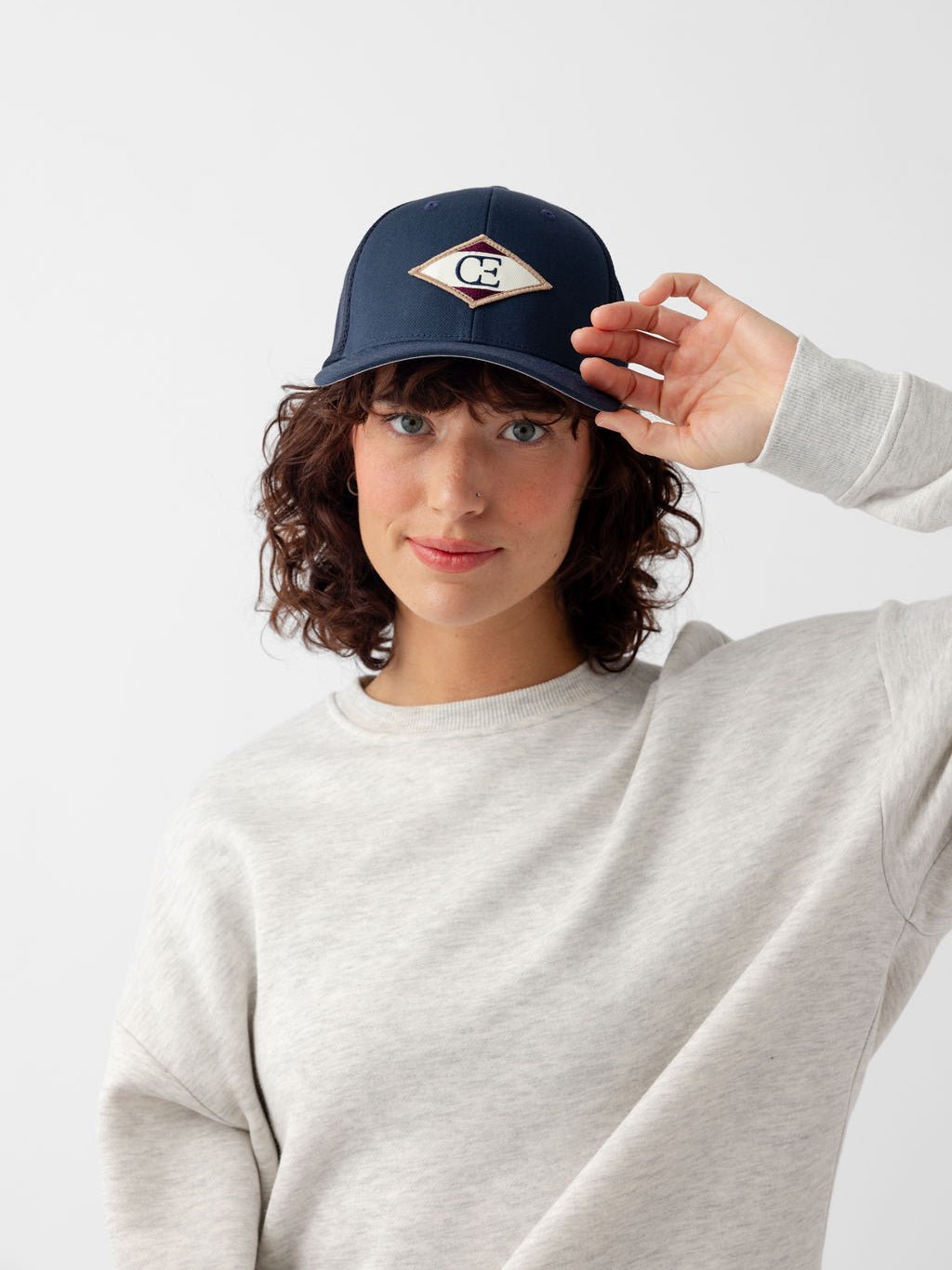 Woman wearing navy diamond mesh trucker hat looking at the camera 