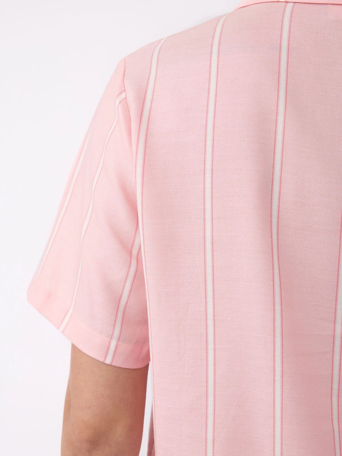 Close-up of a person wearing Cozy Earth's Women's Soft Woven Short Sleeve Pajama Top, featuring light pink with vertical white pinstripes, focusing on the back and shoulder area against a plain white background.