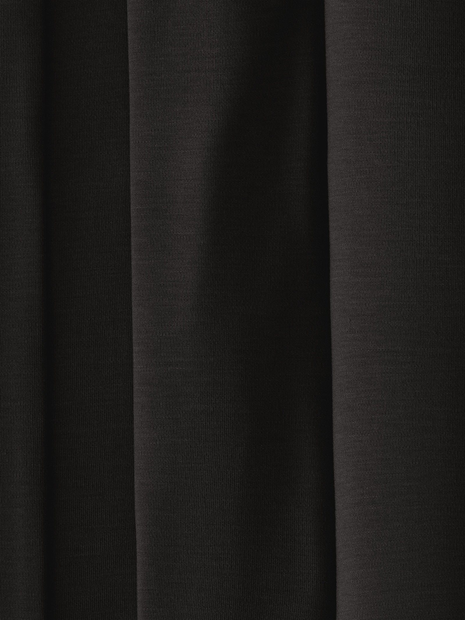 A close-up of dark, evenly folded fabric from the Women's Bedtime Bundle by Cozy Earth, with deep shadows and a smooth texture. The image shows parallel vertical lines formed by the folds, creating an elegant and understated appearance.