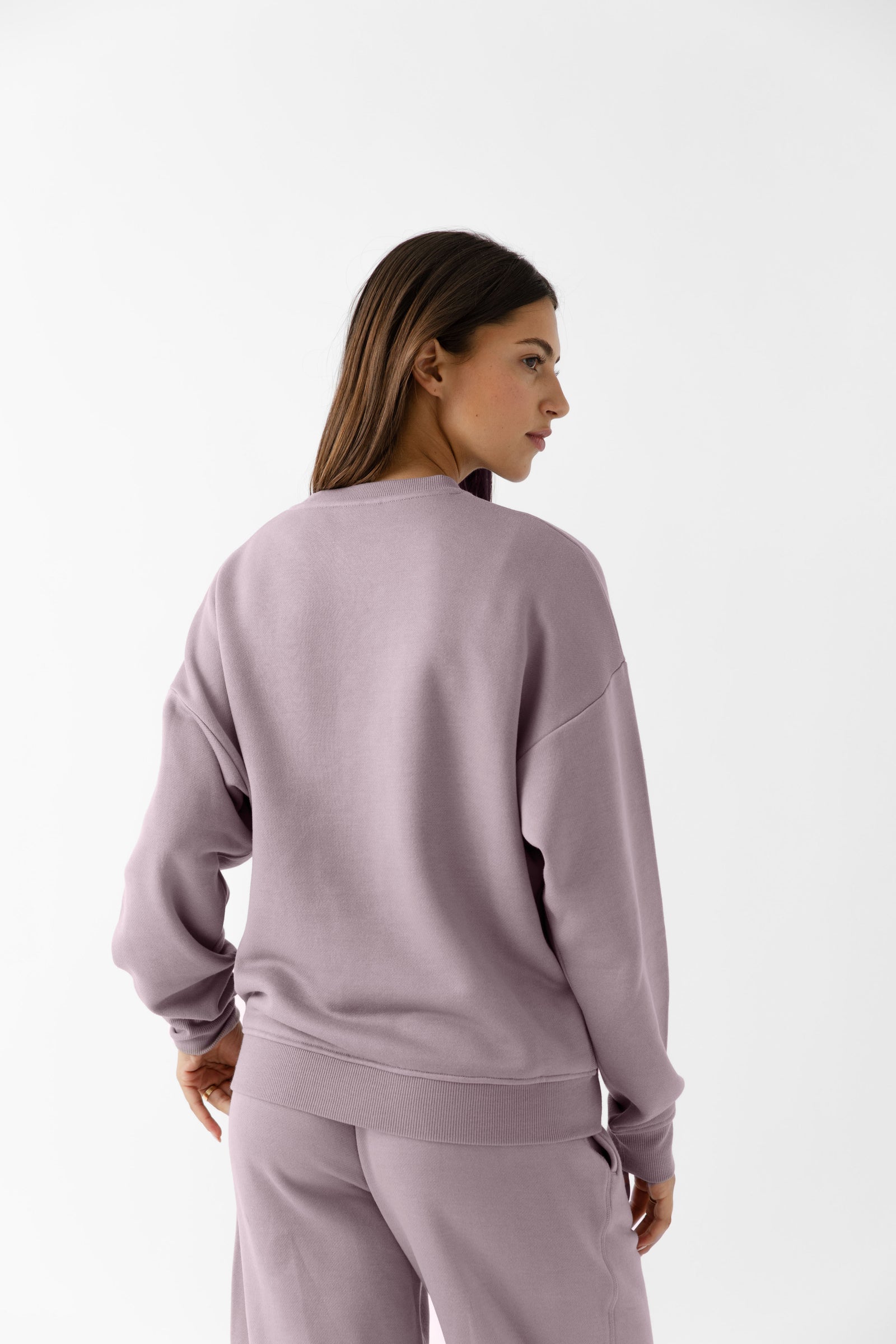 Dusty Orchid CityScape Pullover Crew. The Pullover is being worn by a female model. Accompanying city scape clothing is being worn to complete the look of the outfit. The photo was taken with a white background. 