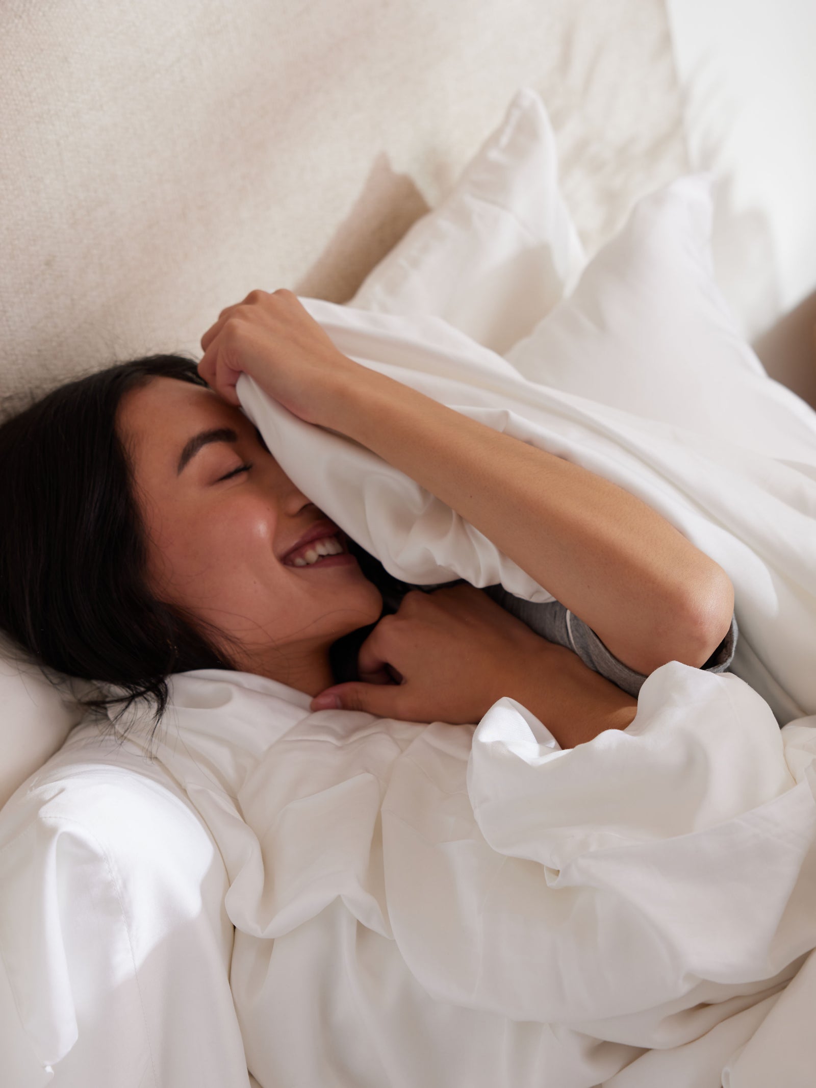 Woman laughing laying down with silk comforter 