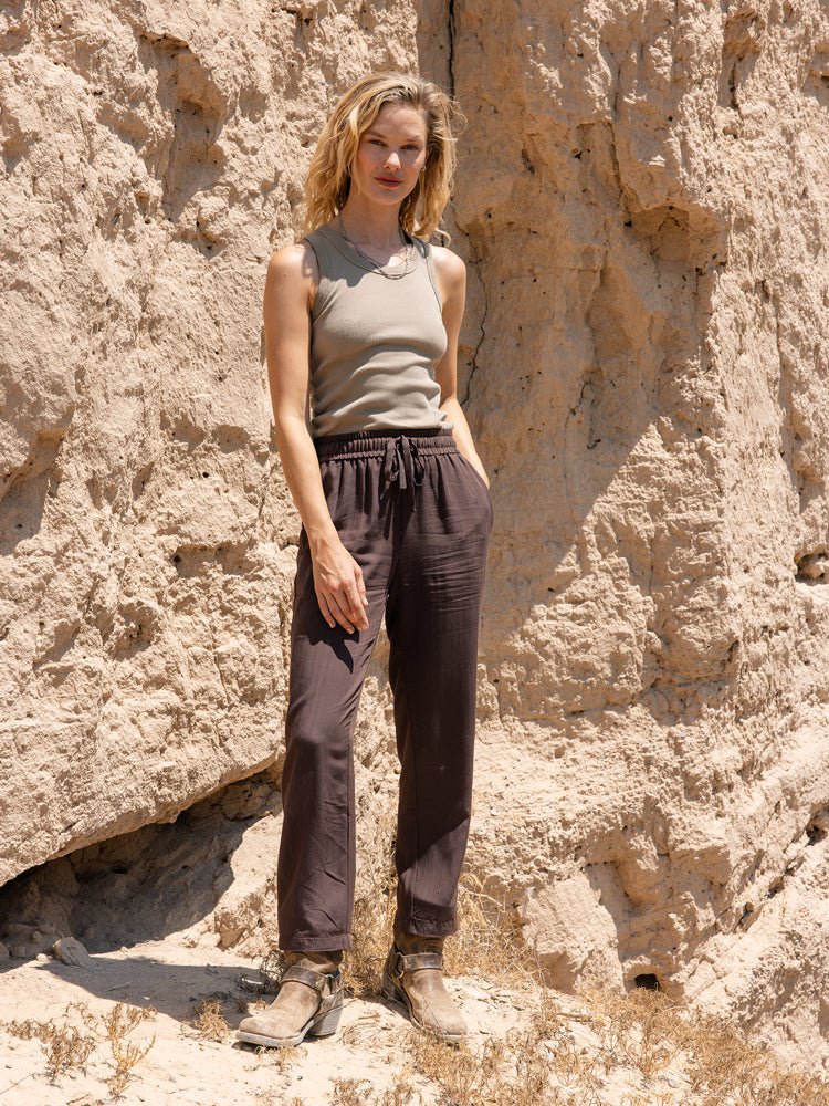 A woman stands against a sunlit cliff, wearing the Cozy Earth Women's Sunset Cropped Pant with her hands in her pockets, looking at the camera.