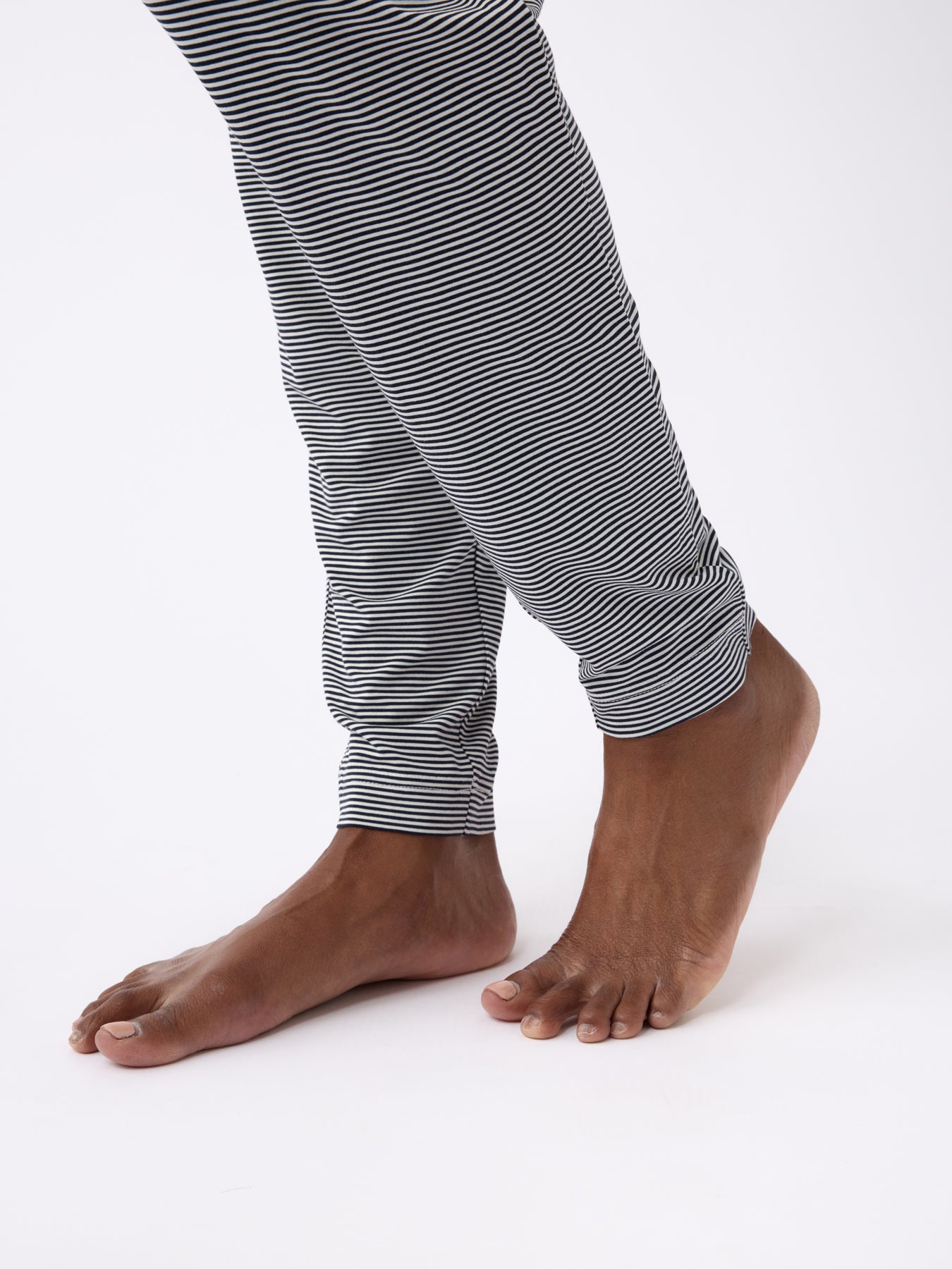 Bare feet step forward in Cozy Earth's Women's Bamboo Stretch-Knit Tapered Pant, featuring black and white stripes with rolled-up cuffs, set against a plain white background.