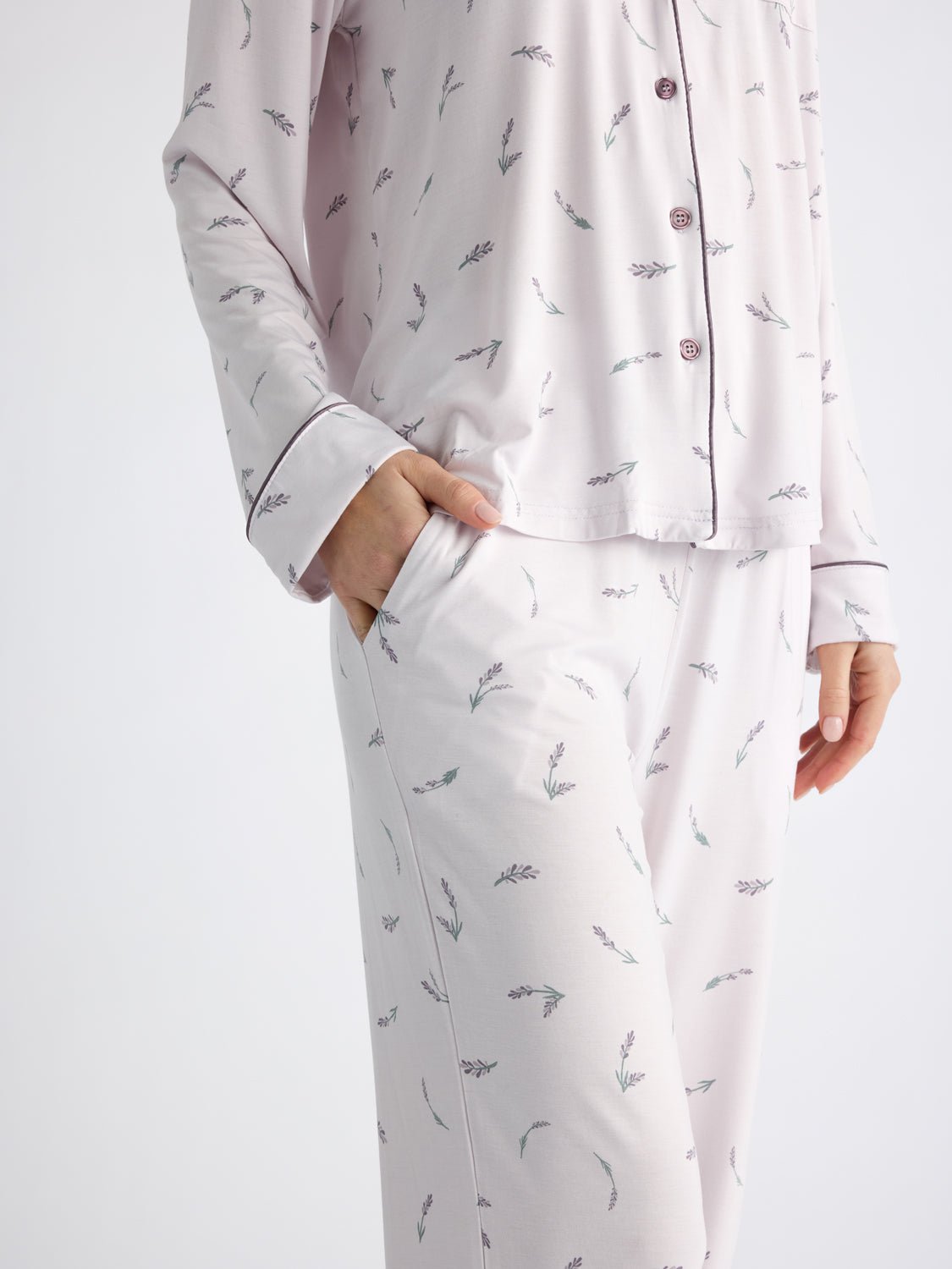 A person wears Cozy Earth Women's Bamboo Stretch-Knit Pajama Pants featuring a subtle branch pattern and matching pajama top with dark piping and buttons, with one hand in the pants pocket. The background is plain white.