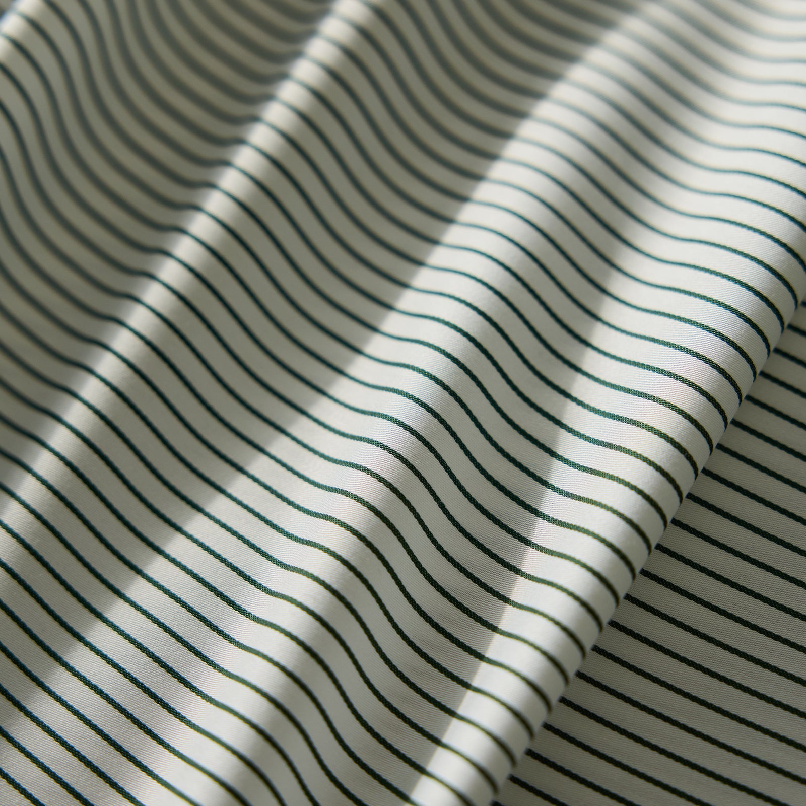 Close-up of the Bamboo Flat Sheet from Cozy Earth, featuring a cream-colored fabric with thin, evenly spaced black stripes. The sheet lies flat with gentle folds, creating soft shadows and highlights.