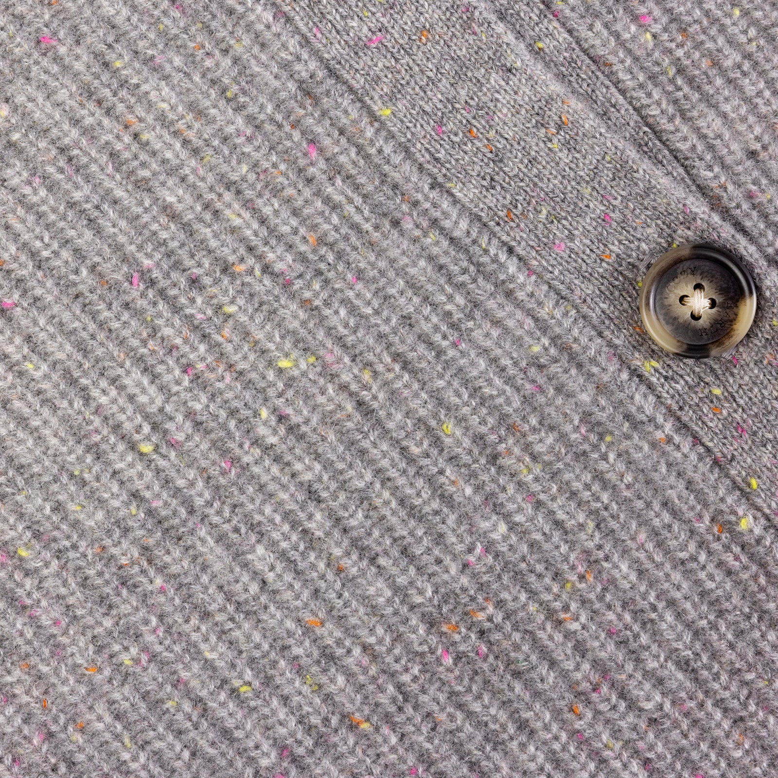 Close-up of a gray tweed fabric from the Oversized Sunday Cashmere Cardigan by Cozy Earth, showcasing its ribbed texture and multicolored specks. A single dark button is visible on the right side of the image, sewn onto the cardigan.