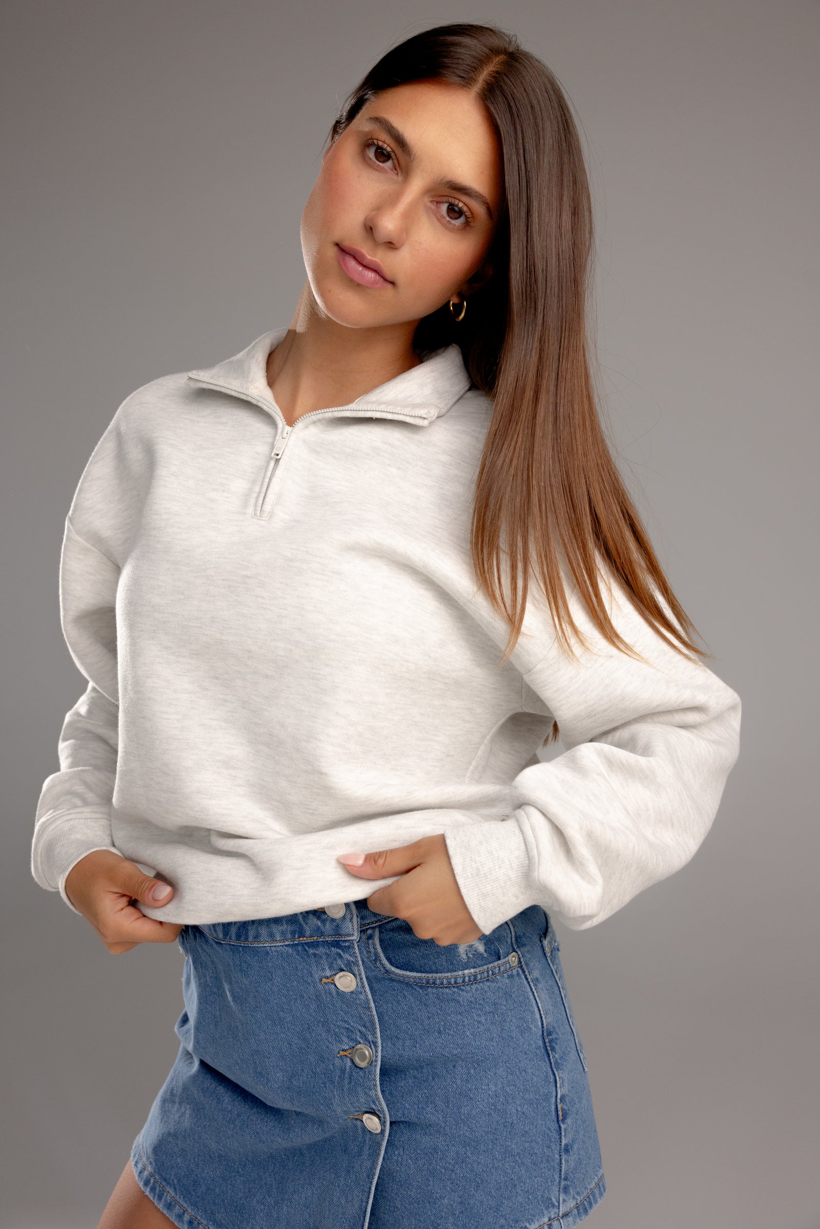 Heather Grey CityScape Quarter Zip. The quarter zip is being worn by a female model. The model is wearing an accompanying jean skirt to complete the look of the quarter zip. The photo was taken with a grey background.