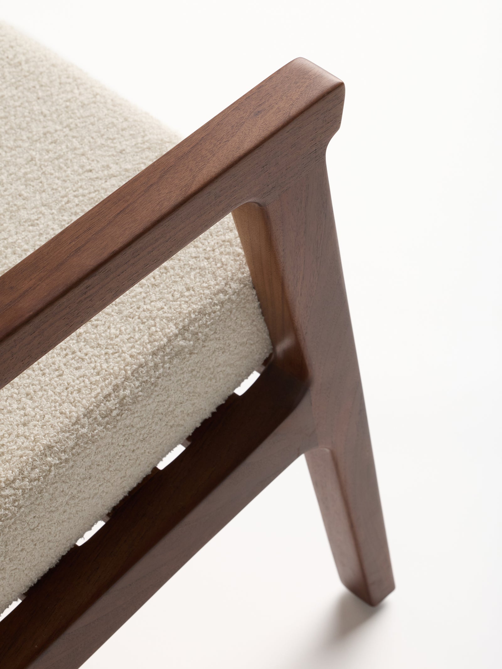 Close-up of the Coronado Lounge Chair by Cozy Earth, featuring a wooden frame and a light textured cushion. The image highlights the armrest and seat corner, showcasing the smooth, elegant design of this mid-century modern furniture piece.