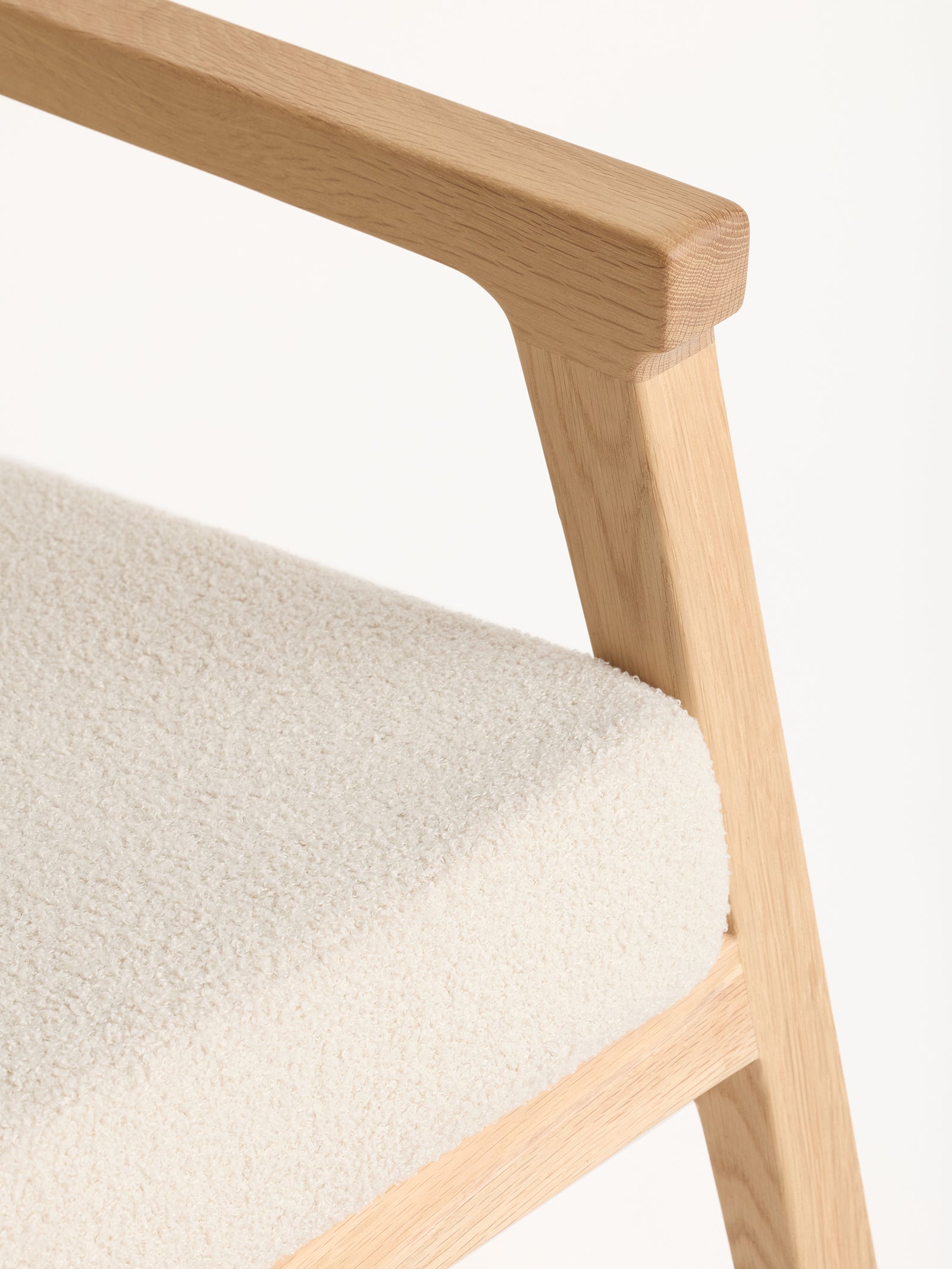 Close-up of the Coronado Lounge Chair from Cozy Earth, featuring a textured light beige fabric seat. The chair's sleek armrest and leg highlight its minimalistic design and craftsmanship against a plain background.