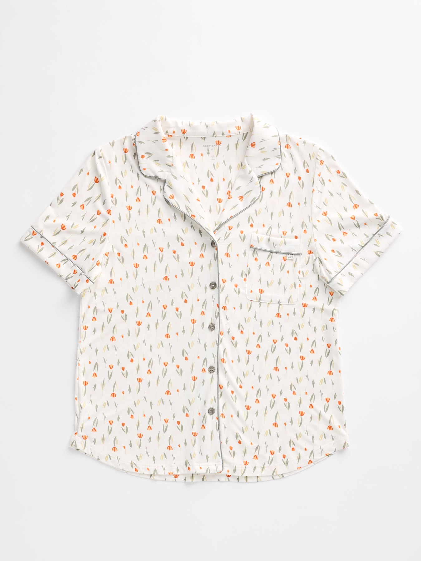Cozy Earth's Women's Bamboo Stretch-Knit Short Sleeve Pajama Set features a white short-sleeved top with an orange and gray floral pattern, a notched collar, black piping, and a single breast pocket.