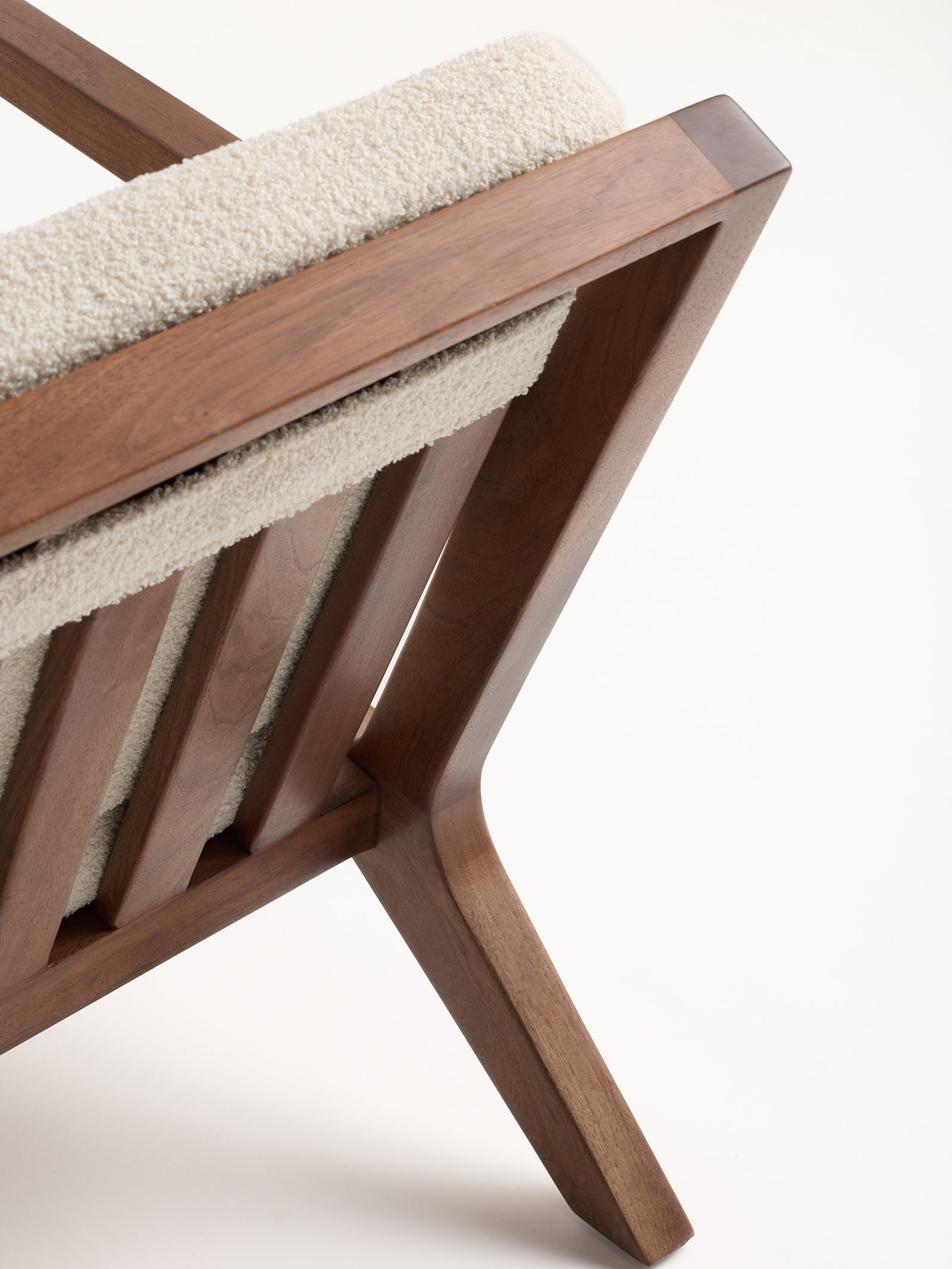 A close-up of the Coronado Lounge Chair by Cozy Earth showcases its minimalist design, featuring a white upholstered backrest. The chair's smooth, angular frame beautifully highlights the natural wood grain against a plain background.