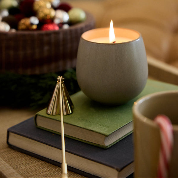 Ceramic candle holder with a lit candle on a surface with a blurred Christmas tree in the background.